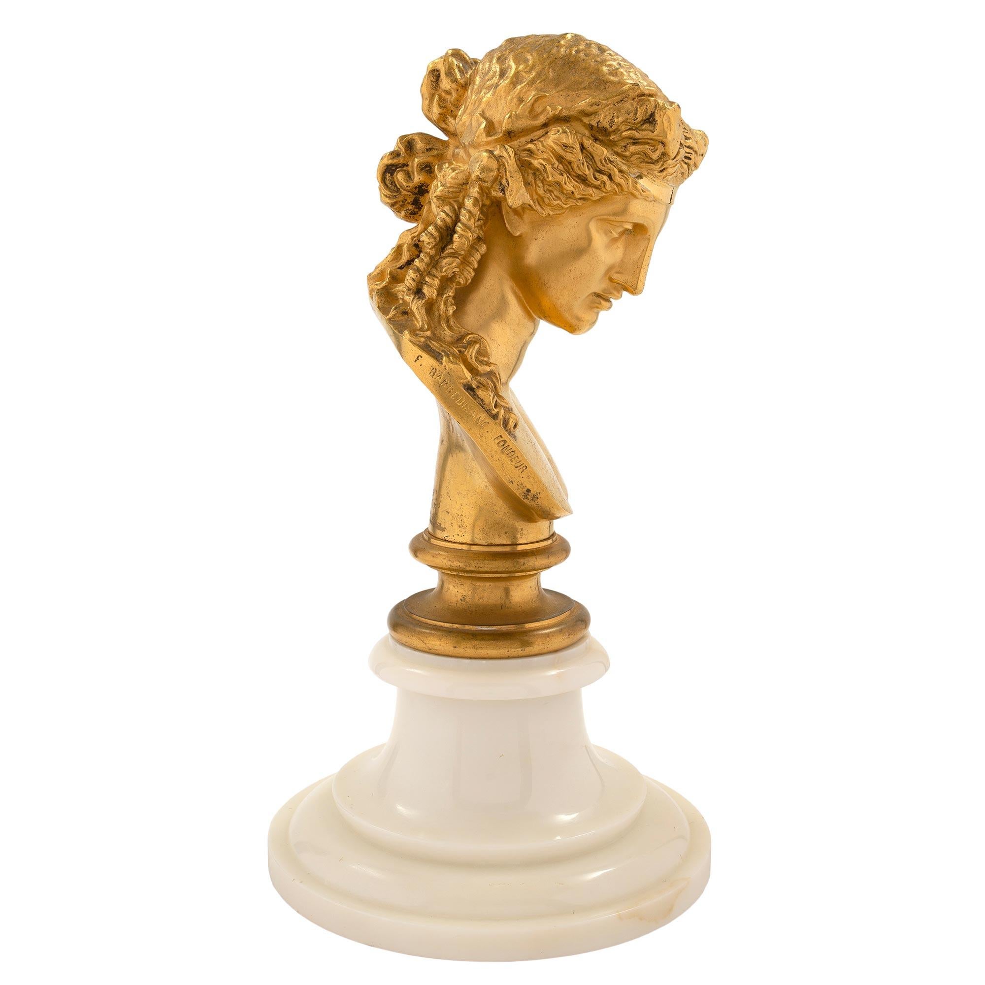 Eine elegante und hochwertige französische Venusbüste aus dem 19. Jahrhundert aus Louis XVI Ormolu, signiert F. BARBEDIENNE FONDEUR. Die Statue wird von einem runden Sockel aus weißem Carrara-Marmor mit Stufenmuster getragen. Oben ist die fein