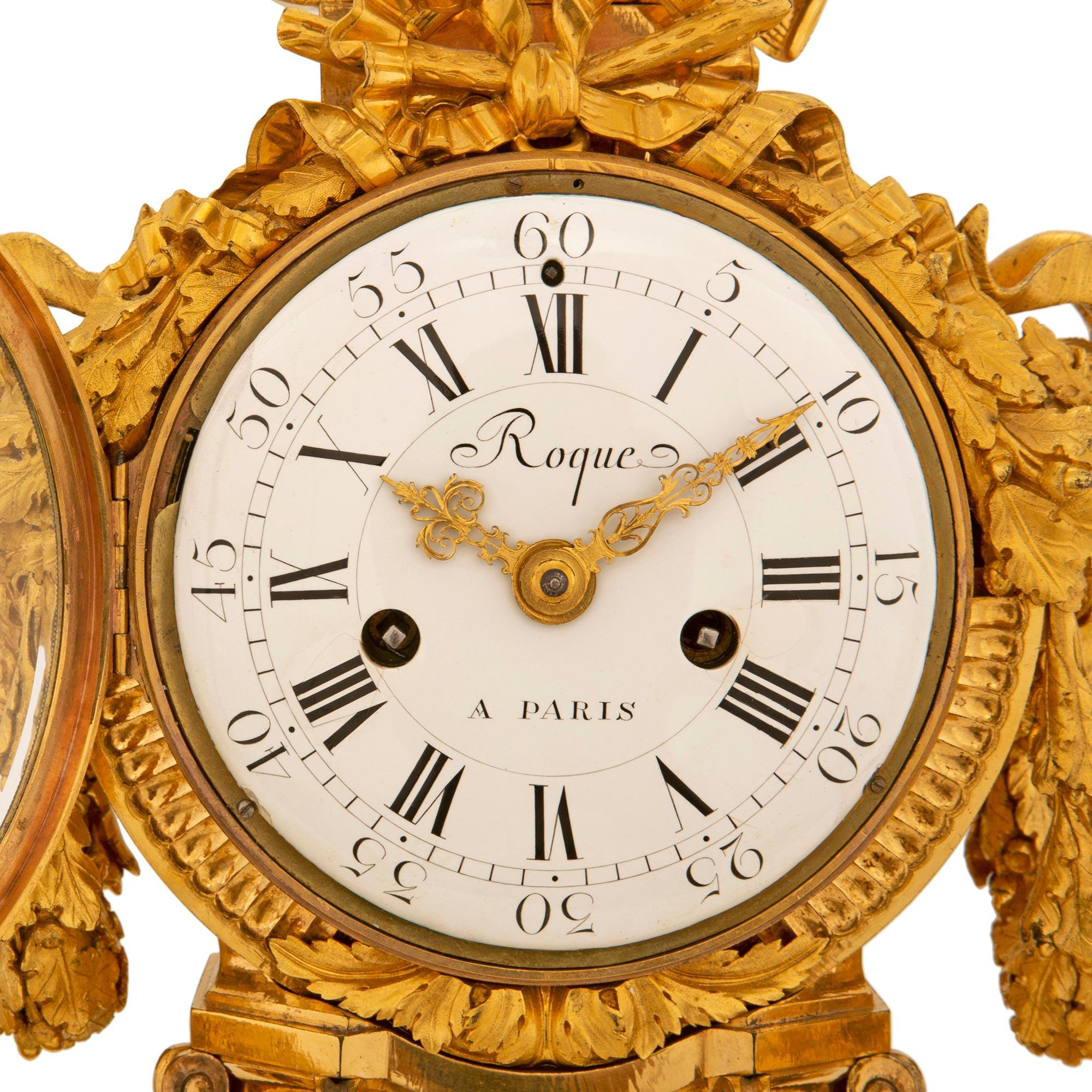 A stunning and most impressive French 19th century Louis XVI st. ormolu clock by Roque, Paris. The clock is raised by elegant circular mottled feet with fine wrap around foliate bands. Above each foot at the white Carrara marble base are striking