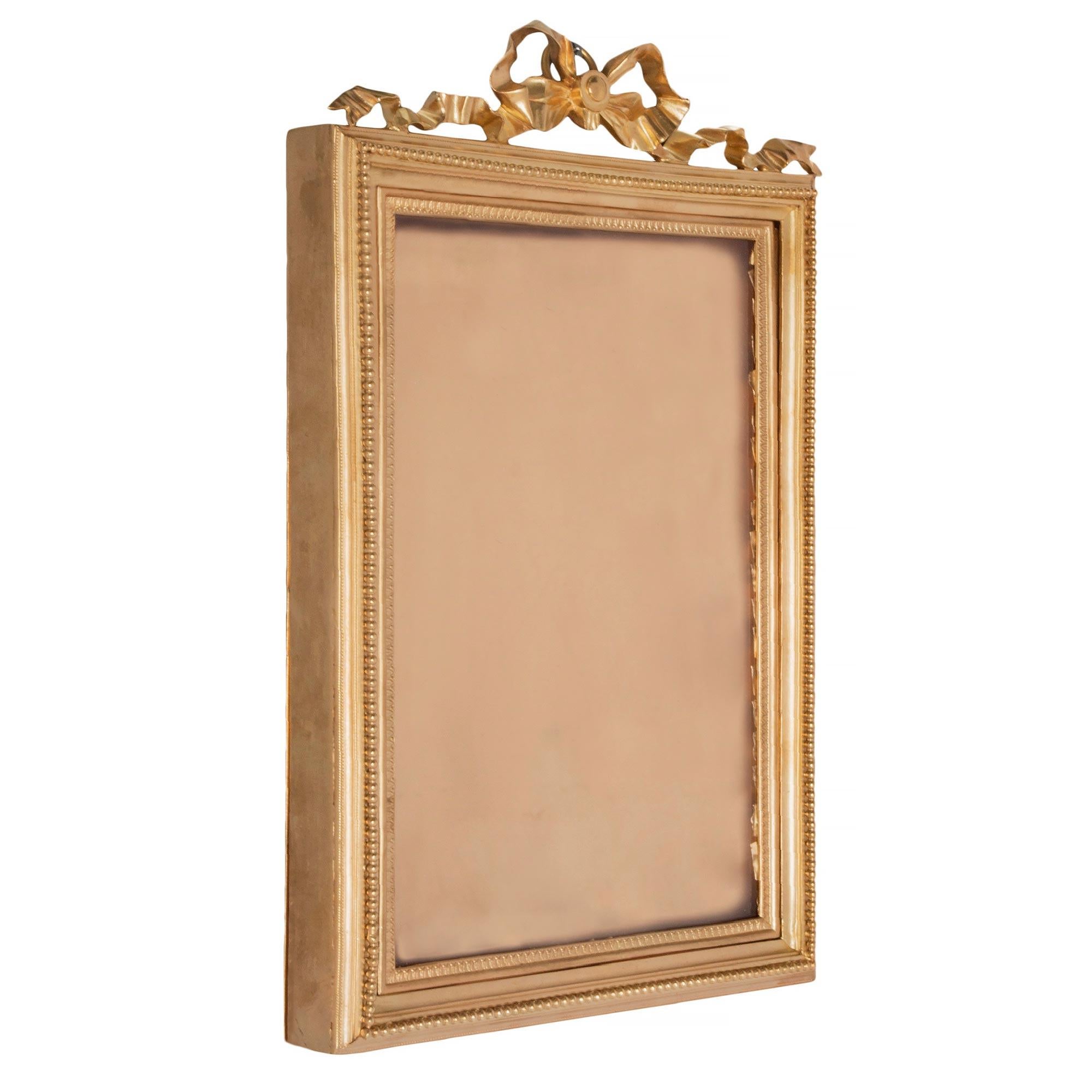 An elegant French 19th century Louis XVI st. ormolu frame. The rectangular frame displays its original glass pane framed within a finely chased Coeur de Rai pattern and beaded design. At the top is a charming and most attractive flowing tied ribbon.