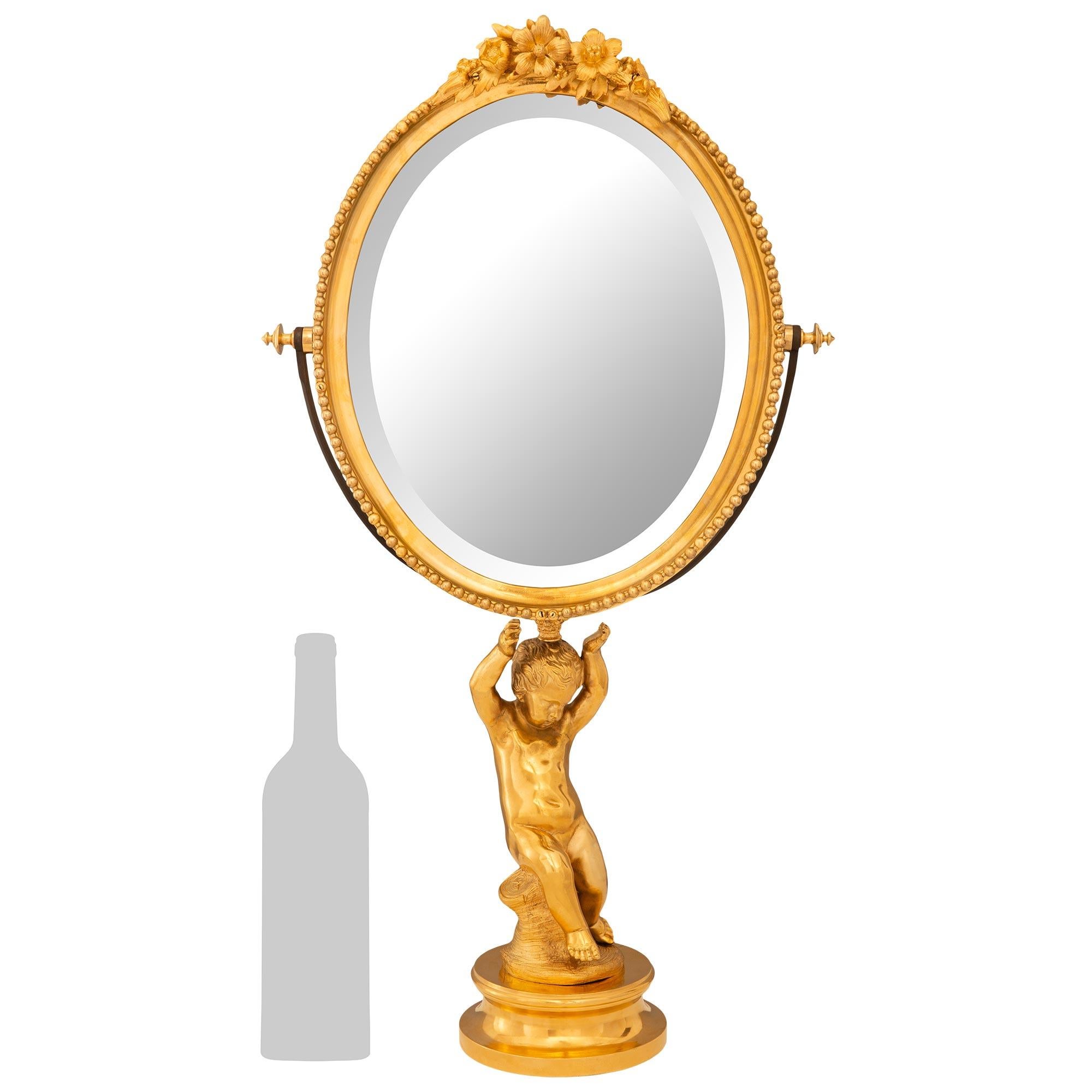 Superbe miroir de courtoisie en bronze doré de haute qualité, de style Louis XVI, datant du 19e siècle. Ce magnifique miroir de courtoisie ovale et biseauté repose sur un piédestal circulaire à gradins surmonté d'un chérubin assis sur une souche