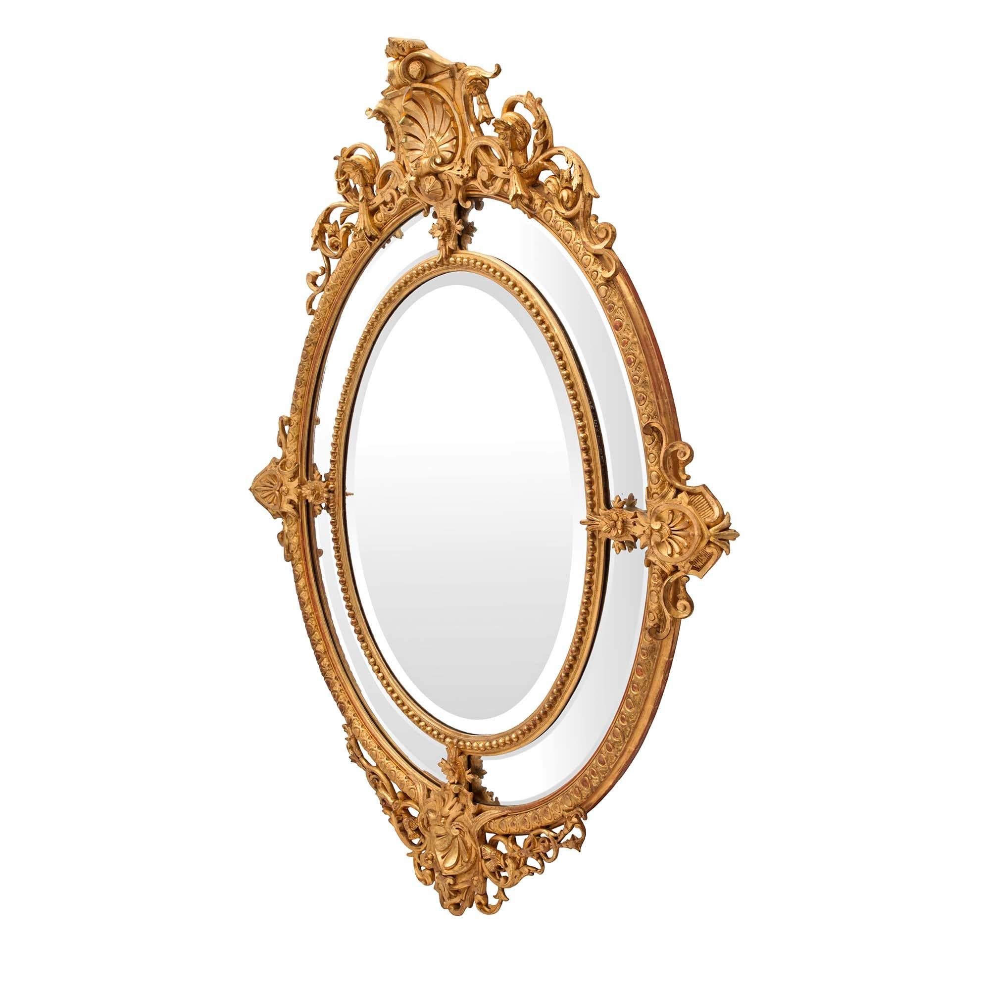 Un beau miroir français du 19ème siècle, de style Louis XVI, à double cadre ovale en bois doré. La plaque de miroir biseautée d'origine est encadrée d'une fine bordure perlée. Les quatre plaques de miroir biseautées d'origine, de forme arquée, sont