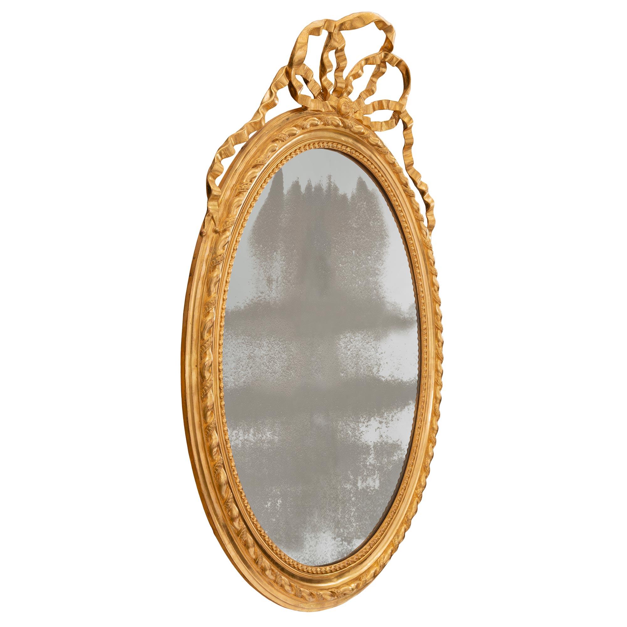 Très élégant miroir ovale en bois doré de style Louis XVI du XIXe siècle. La plaque de miroir d'origine est encadrée d'une jolie bordure perlée et mouchetée. Le bord est orné d'un fin motif torsadé qui se prolonge dans tout le cadre. Ci-dessus, un