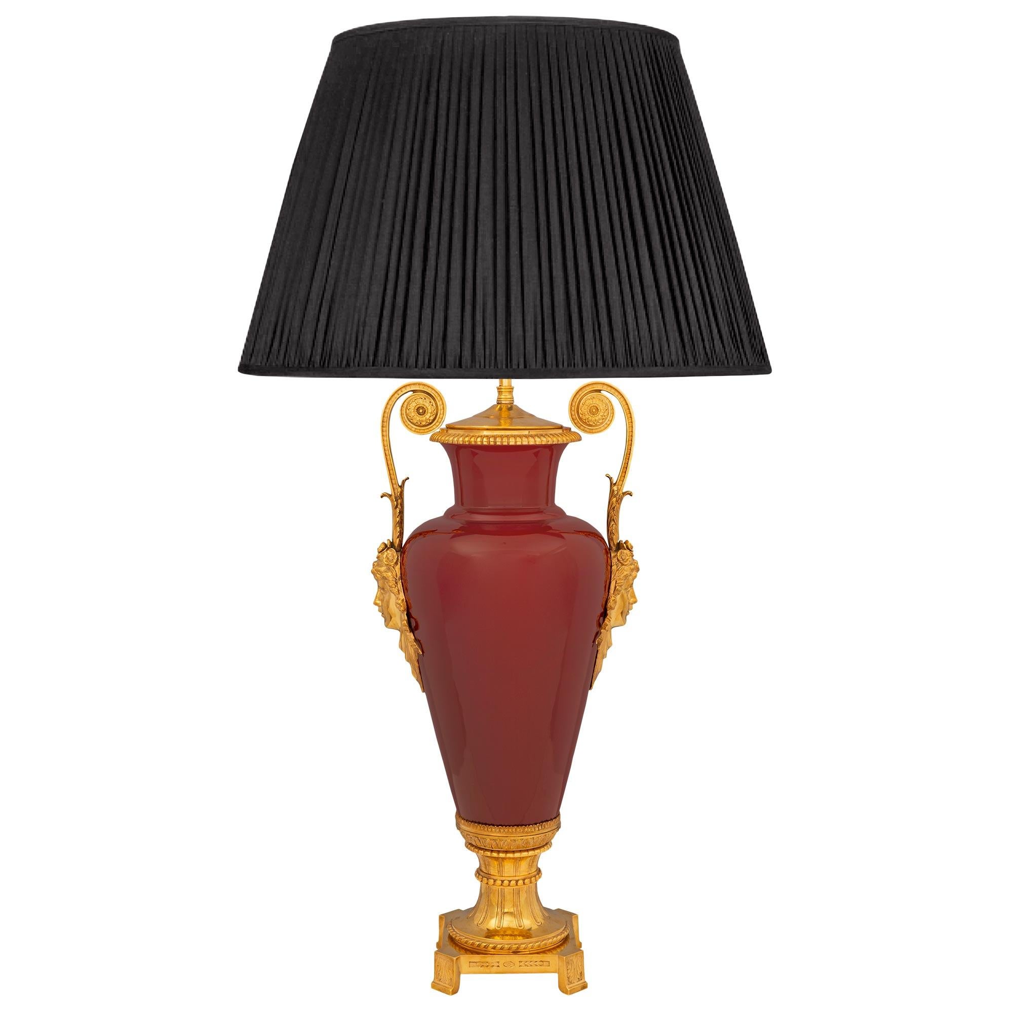 A large scale and most elegant French 19th century Louis XVI st. oxblood red porcelain and ormolu lamp. The lamp is raised by a square ormolu base with cut corners, foliate feet, and a fluted socle shaped pedestal support with fine beaded and