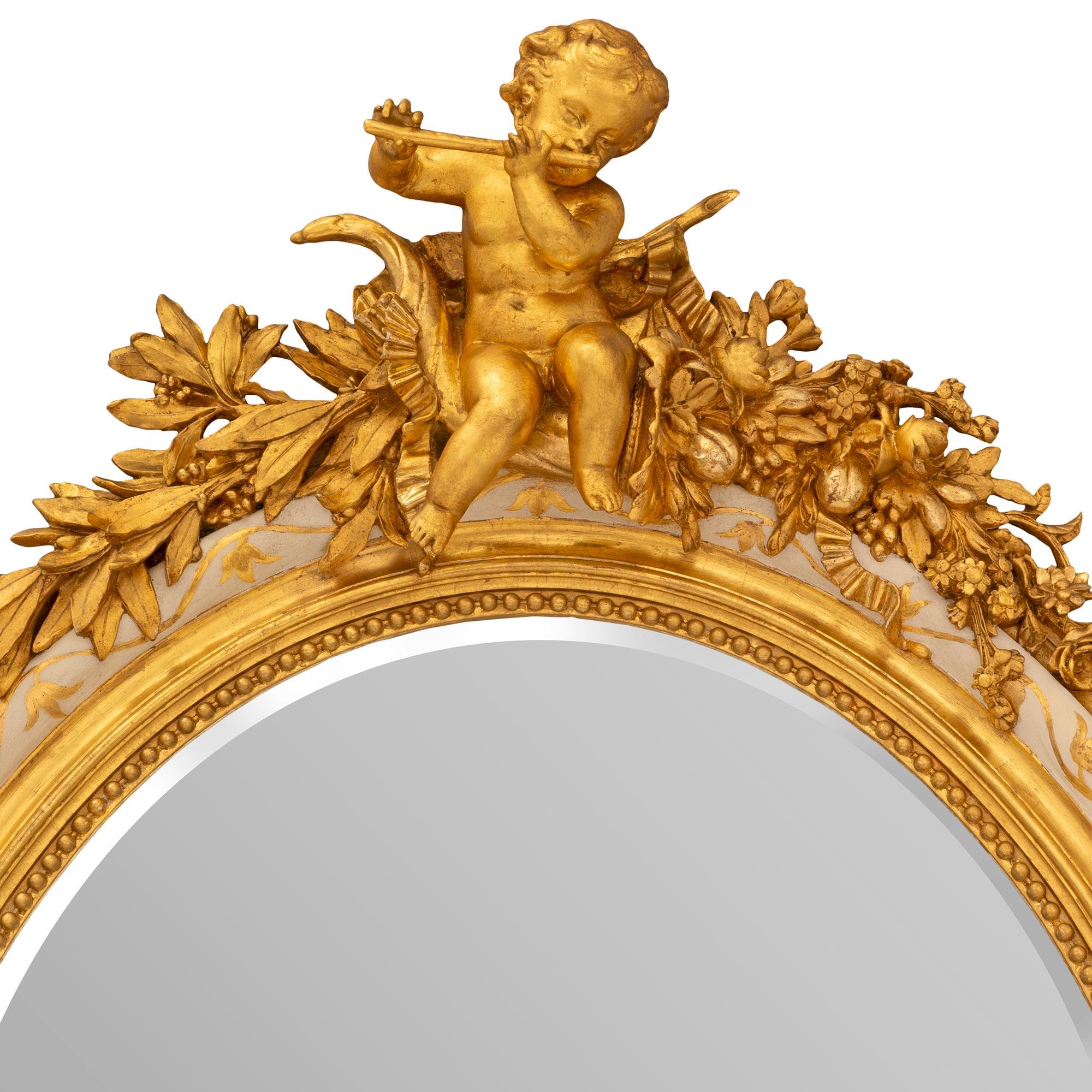 A striking French 19th century Louis XVI st. patinated and giltwood mirror. The oval mirror retains its original mirror plate set within a beautiful wrap around beaded and mottled band with most decorative giltwood scrolled foliate designs extending