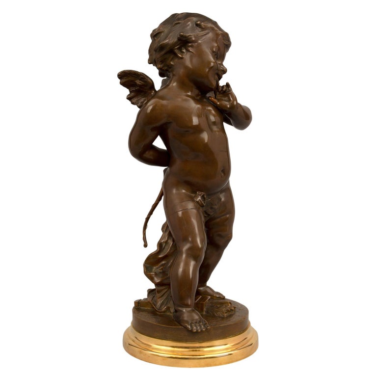 A most charming and high quality French 19th century Louis XVI st. patinated bronze and ormolu statue, signed E Drouot. The statue is raised by a circular ormolu base with a mottled border. The finely detailed winged cherub, possibly Cupid, is
