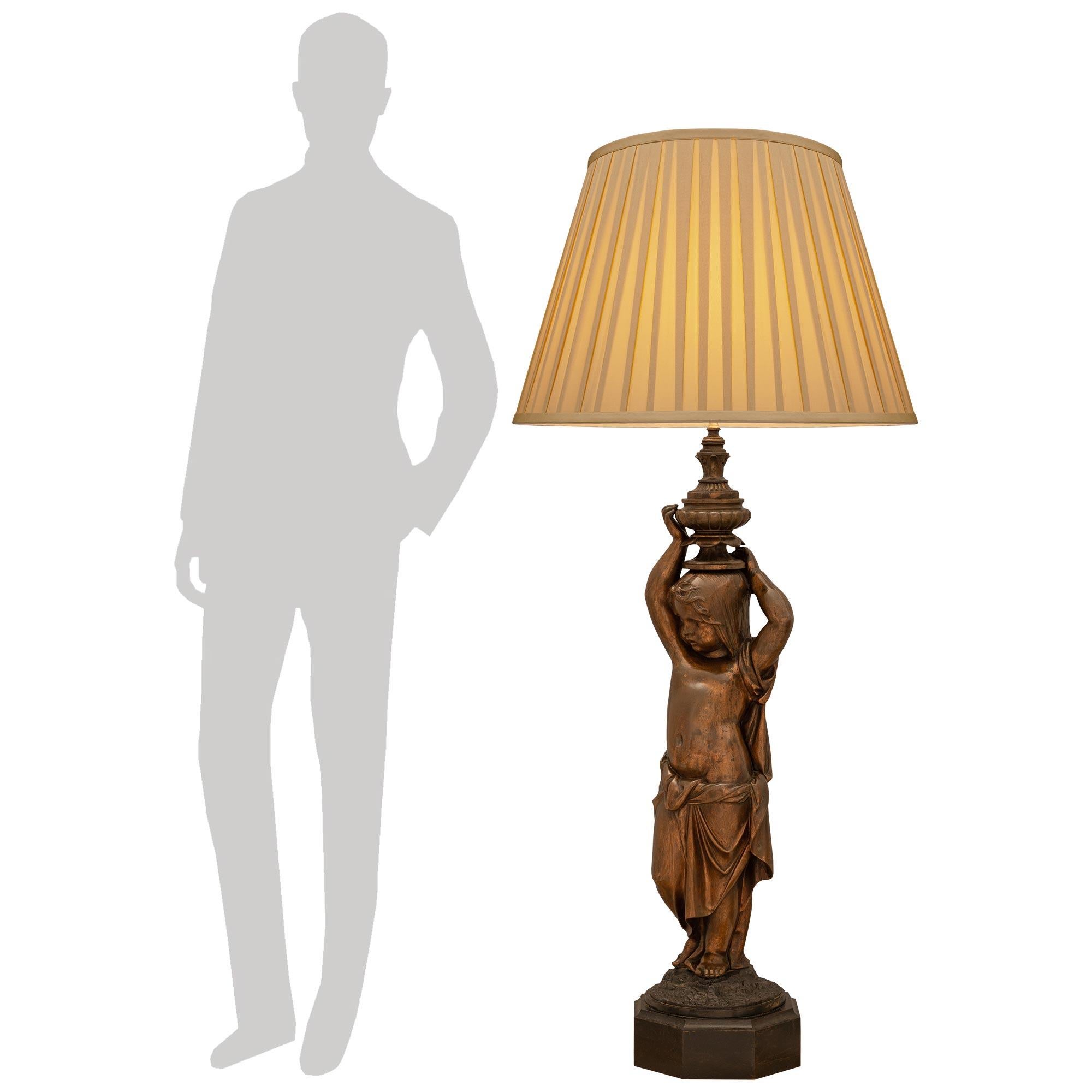 Impressionnante lampe en bronze patiné de style Louis XVI du XIXe siècle. Cette magnifique lampe, qui a conservé toute sa patine d'origine, repose sur une base octogonale surmontée d'une plate-forme circulaire et terrestre qui supporte le chérubin.