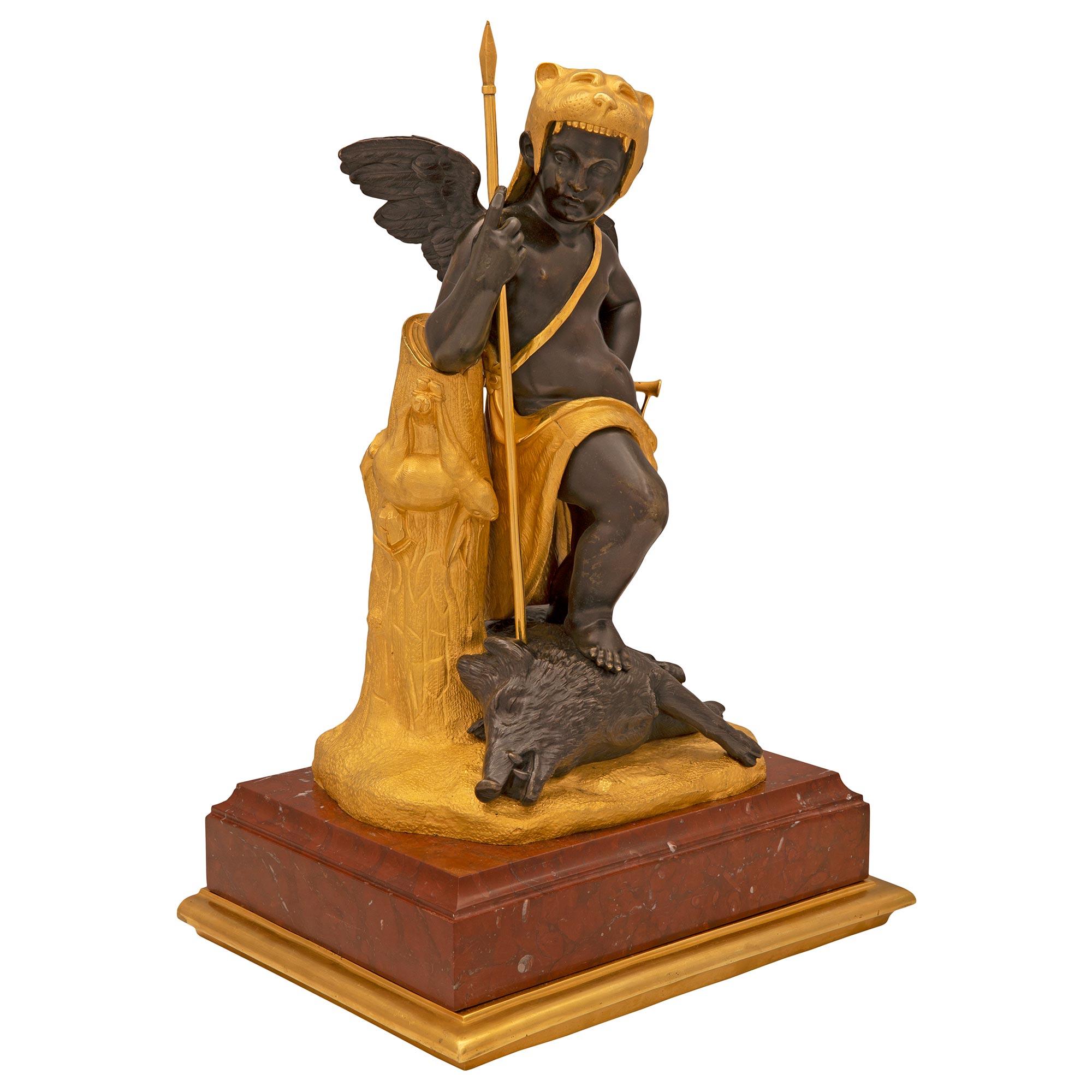 A striking French 19th century Louis XVI st. patinated bronze, ormolu, and Rouge Griotte marble statue. The statue is raised by a square Rouge Griotte marble base with a most elegant mottled ormolu band. At the center is a charming young winged