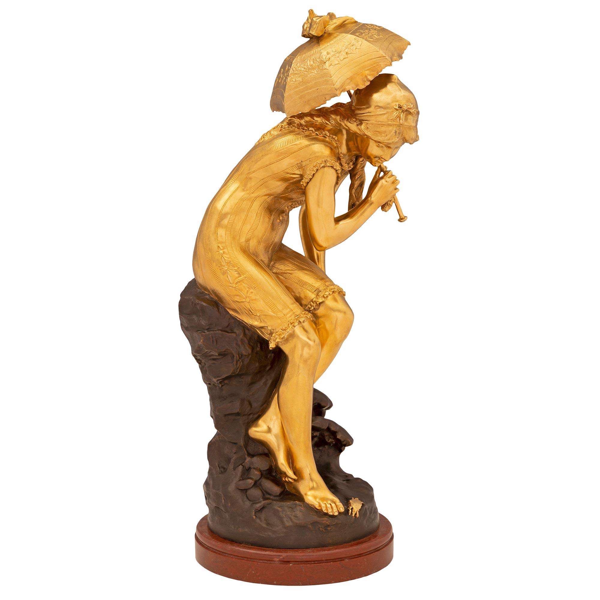 Charmante statue de style Louis XVI du XIXe siècle en bronze patiné, bronze doré et marbre Rouge Griotte, signée Moreau. La statue est surélevée par un socle circulaire en marbre Rouge Griotte avec une fine bande tachetée enveloppante. Au-dessus, on