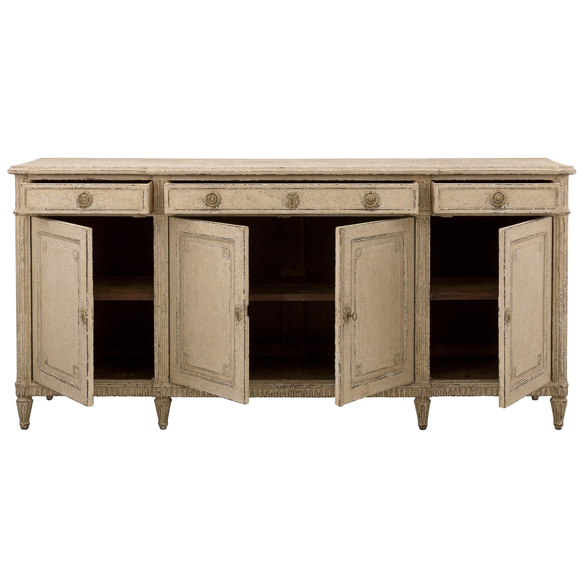 An elegant French 19th century Louis XVI st. patinated buffet. The four door three drawer buffet is raised by six circular tapered fluted legs below the straight fluted frieze. Each drawer displays a most decorative mottled recessed design with fine