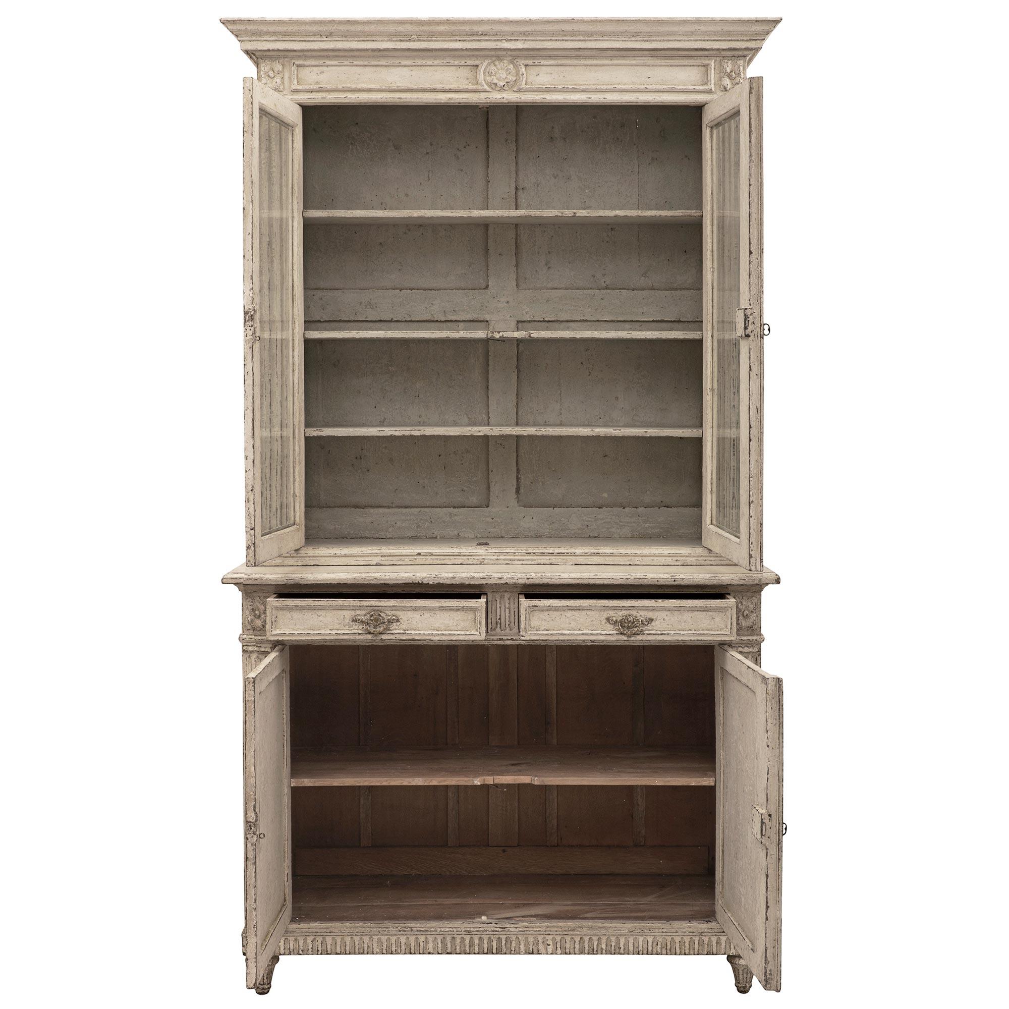 An elegant French 19th century Louis XVI st. patinated wood cabinet vitrine. The four door two drawer Deux Corps vitrine is raised by fine tapered fluted topie shaped feet below the lovely fluted straight frieze. The two bottom doors each display