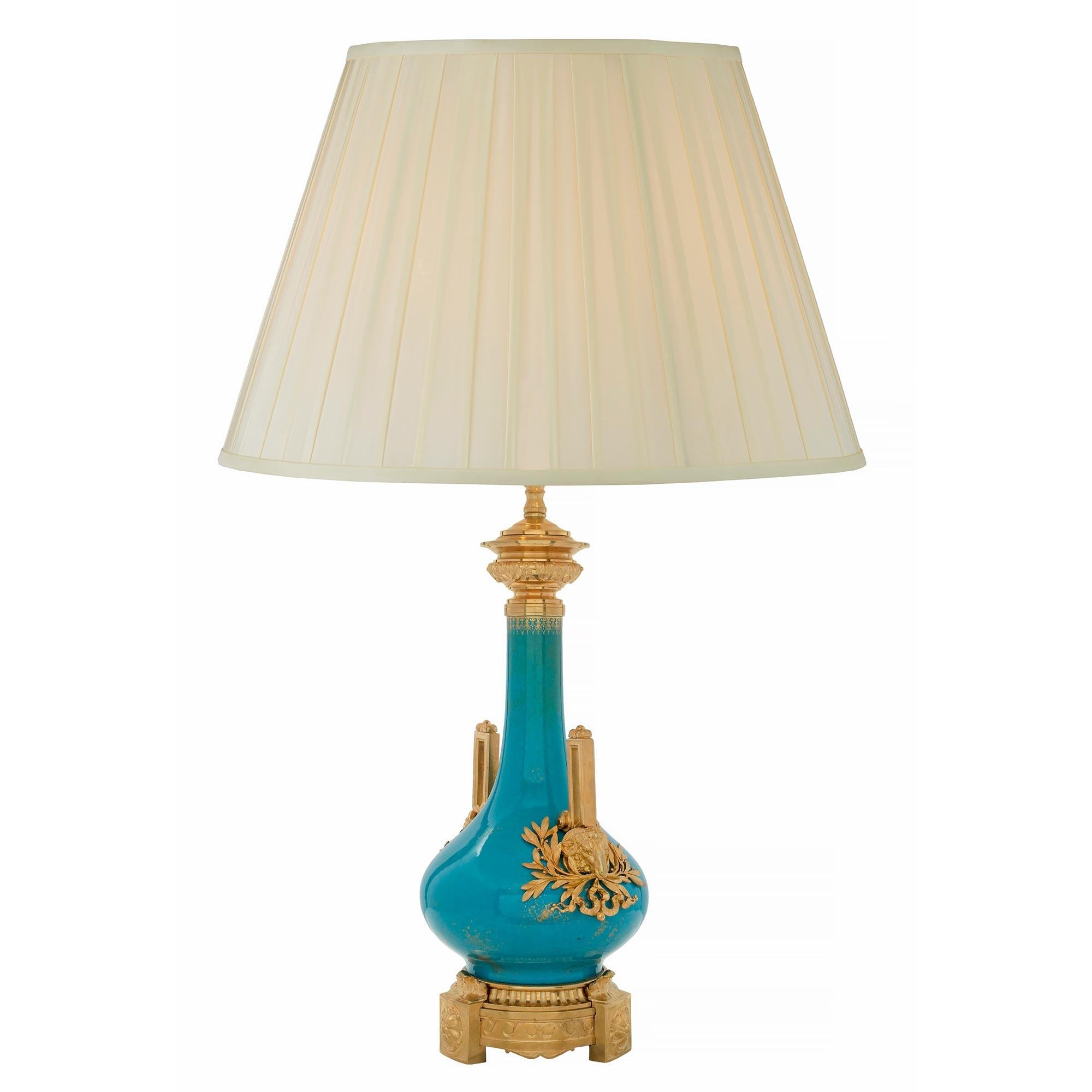 Une magnifique lampe française du 19ème siècle en porcelaine et bronze doré de style Louis XVI. La lampe est surélevée par une base circulaire en bronze doré avec des pieds à rosettes en blocs saillants très décoratifs, flanqués de volutes de