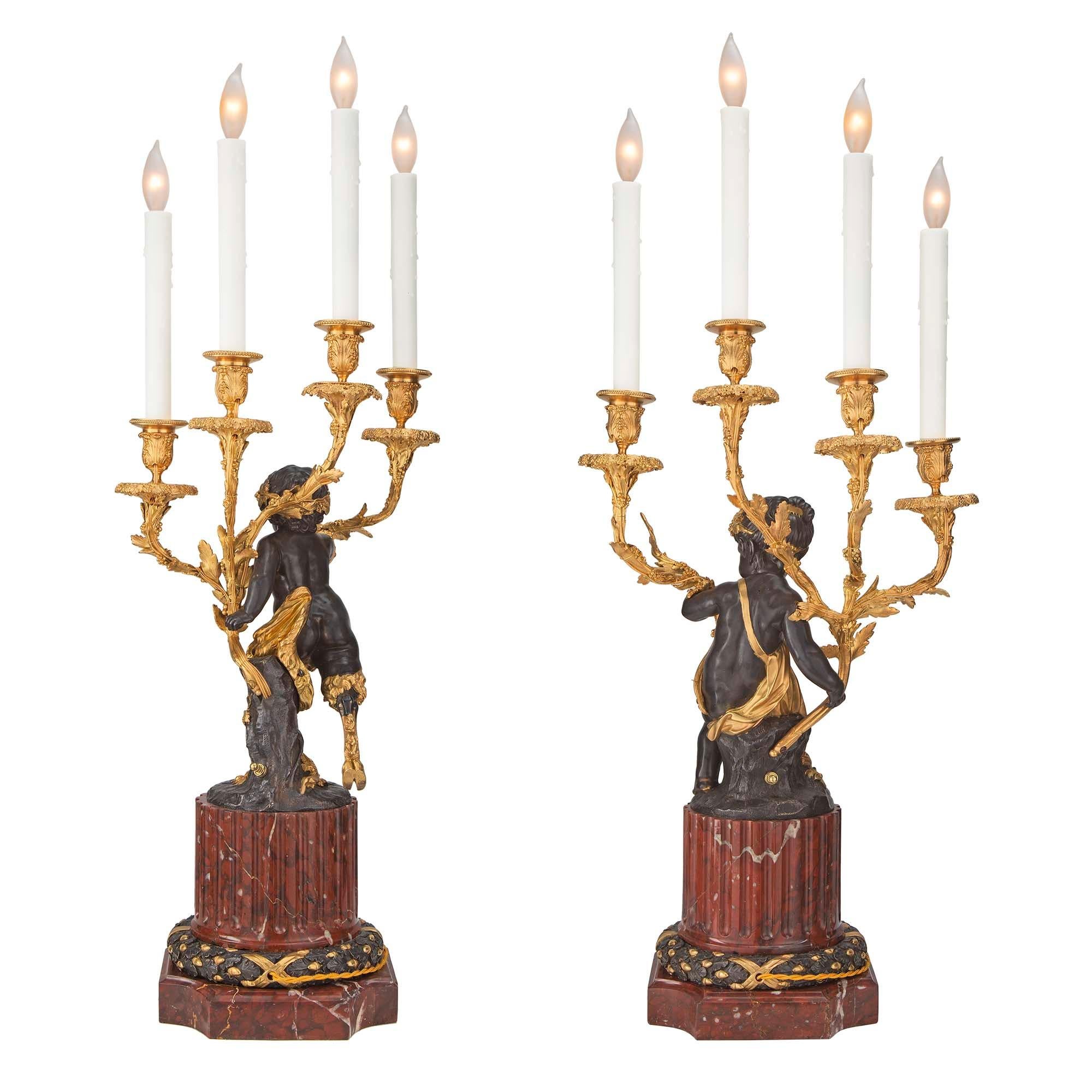 A charming and high quality true pair of French 19th century Louis XVI st. Rouge Griotte marble, patinated bronze, and ormolu four arm candelabras mounted into lamps. Each lamp is raised by a square base with concave corners below a striking
