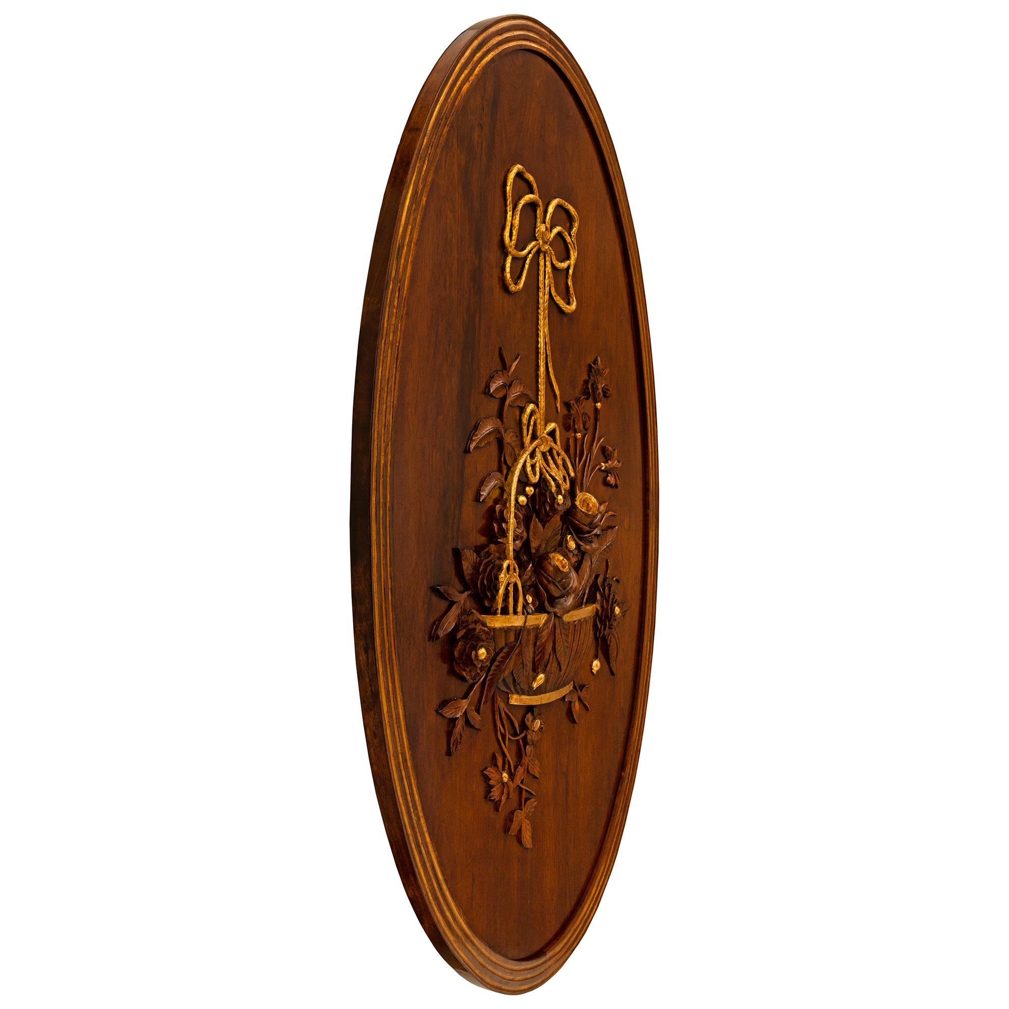 A charming and extremely decorative French 19th century Louis XVI st. Walnut and Giltwood wall decor/plaque. The large scale oval plaque displays an elegant frame with Giltwood fluted bands continuing around the entirety of the frame and centering