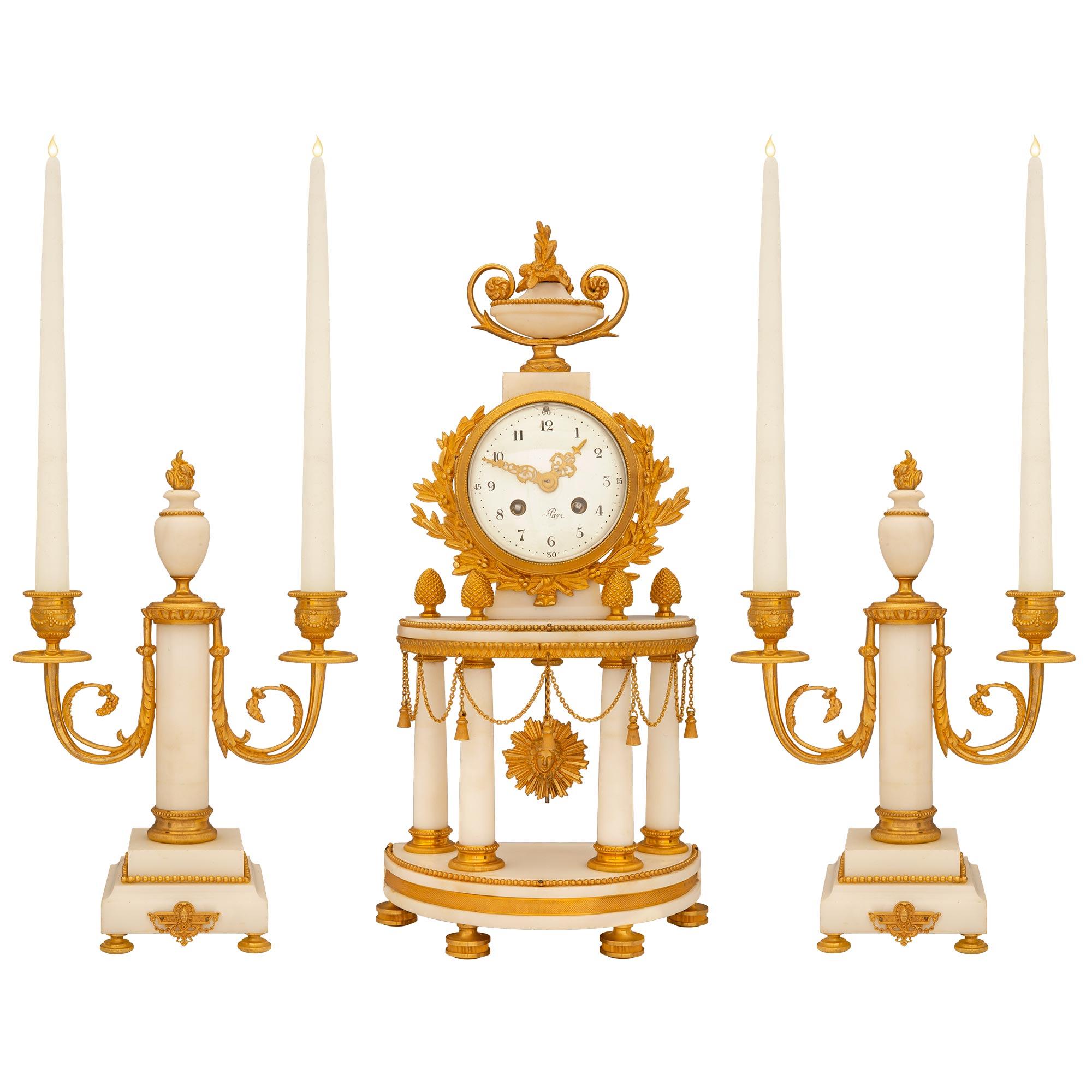 An impressive French 19th century Louis XVI st. ormolu mounted on white Carrara marble clock Garniture set. The three piece set includes a pair of two arm candelabras ormolu mounted with beads and C scrolled arms. The clock is ornamented with ormolu