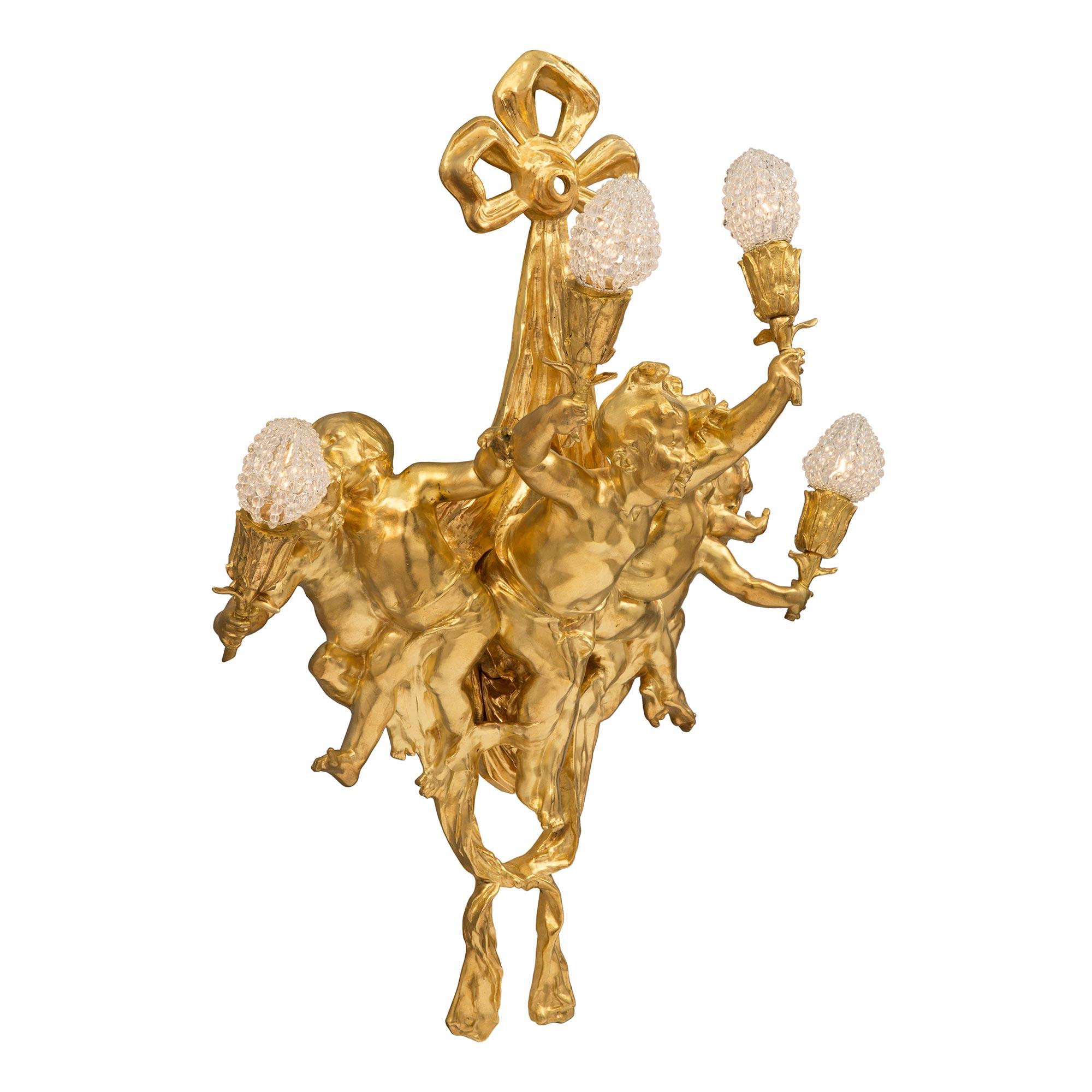 A striking French 19th century Louis XVI style Belle Époque Period four arm ormolu sconce. The sconce is centered by a lovely bottom tied swaging fabric. At the center are five most charming richly chased cherubs dancing and playing, while holding