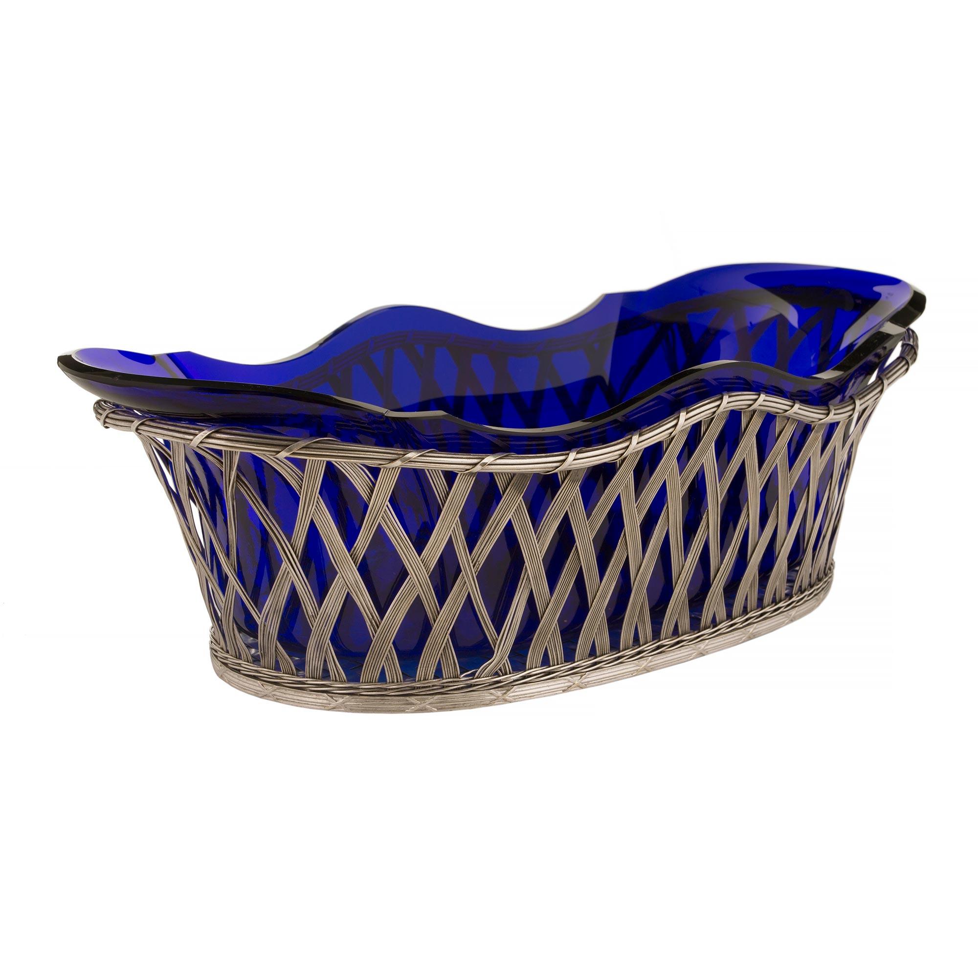 An elegant French 19th century Louis XVI st. silvered bronze centerpiece with a cobalt blue glass insert. The oval shaped centerpiece has a weave design with a scalloped shape. The basket has an X decoration at the base and a spiral looped top