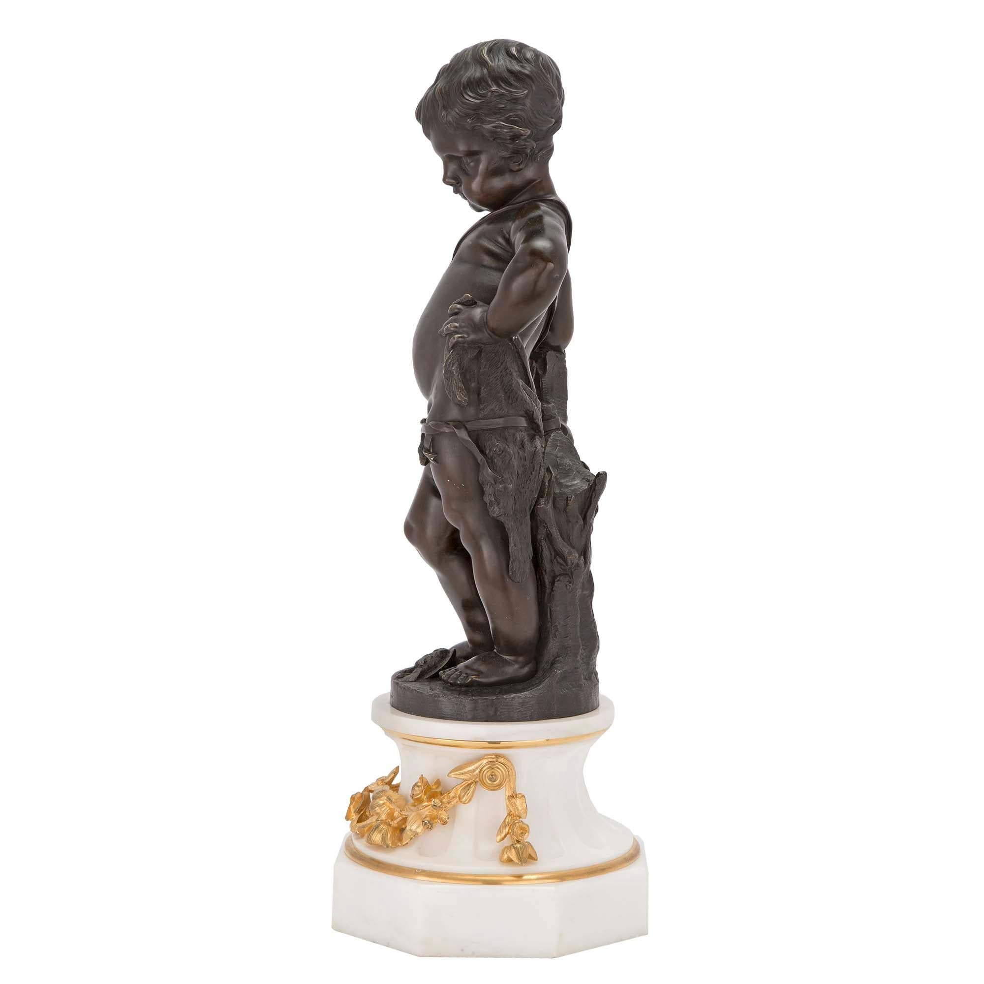 Charmant putti en bronze patiné de style Louis XVI du XIXe siècle, en robe de chasse. La statue repose sur une très élégante base octogonale en marbre blanc de Carrare qui se rétrécit jusqu'à un socle cannelé décoré de guirlandes florales en bronze