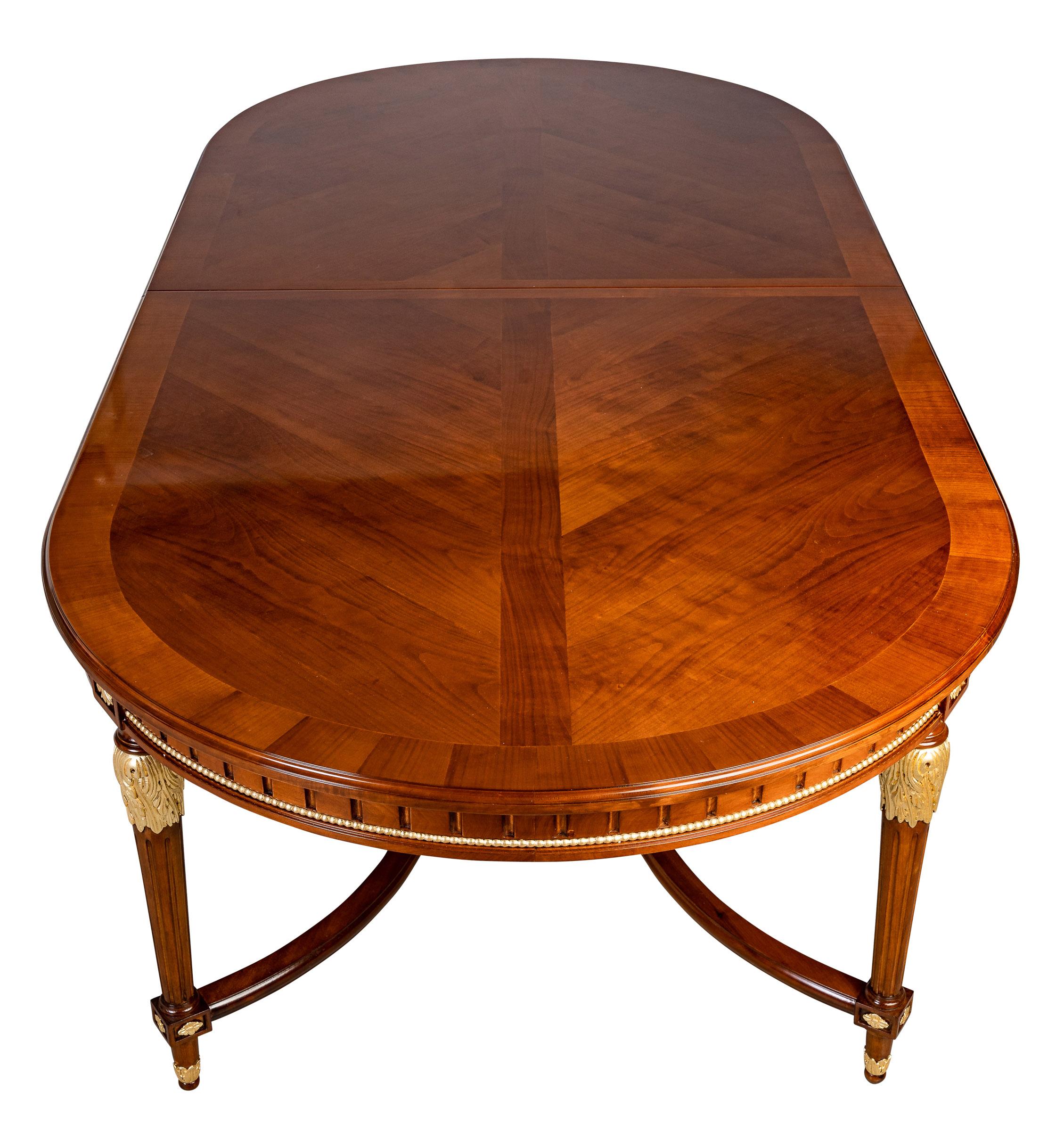 An exquisite French 19th century Louis XVI style dining table with two extensions. The table is raised by Impressive circular fluted tapered legs. Each leg is decorated with leaves and original gilding. The entire top has a wonderful cherry patina