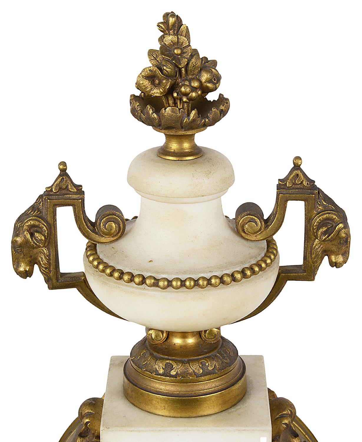 French 19th century Louis XVI style white marble and gilded ormolu clock garniture, having a two handled urn finial above a white enamel clock face, an eight day duration clock that strikes on the hour and half hour. Flanked by a matching pair of