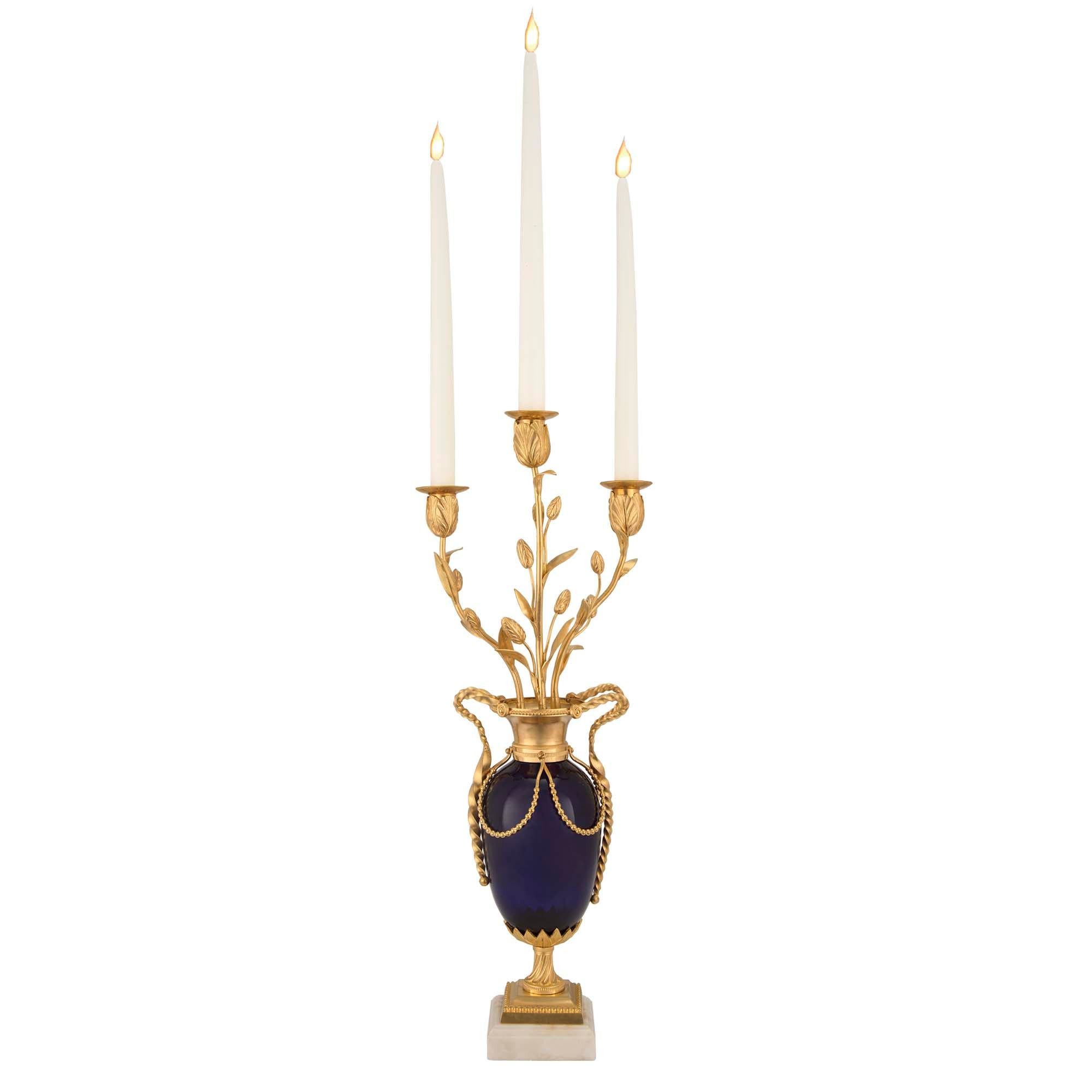A very elegant pair of French mid 19th century Louis XVI st. cobalt blue glass, ormolu and white Carrara marble three arm candelabras. Each candelabra is raised on a white Carrara marble and ormolu base below the ormolu support, accented with a