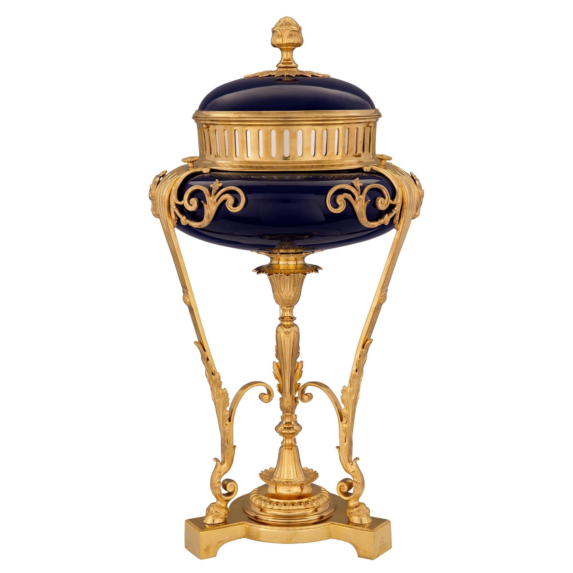 A superb French 19th Century Louis XVI st. cobalt blue Sèvres porcelain centerpiece. The centerpiece is modeled after a brule parfum and raised by a triangular base with three most elegant lightly curved legs with hoof feet and large richly chased