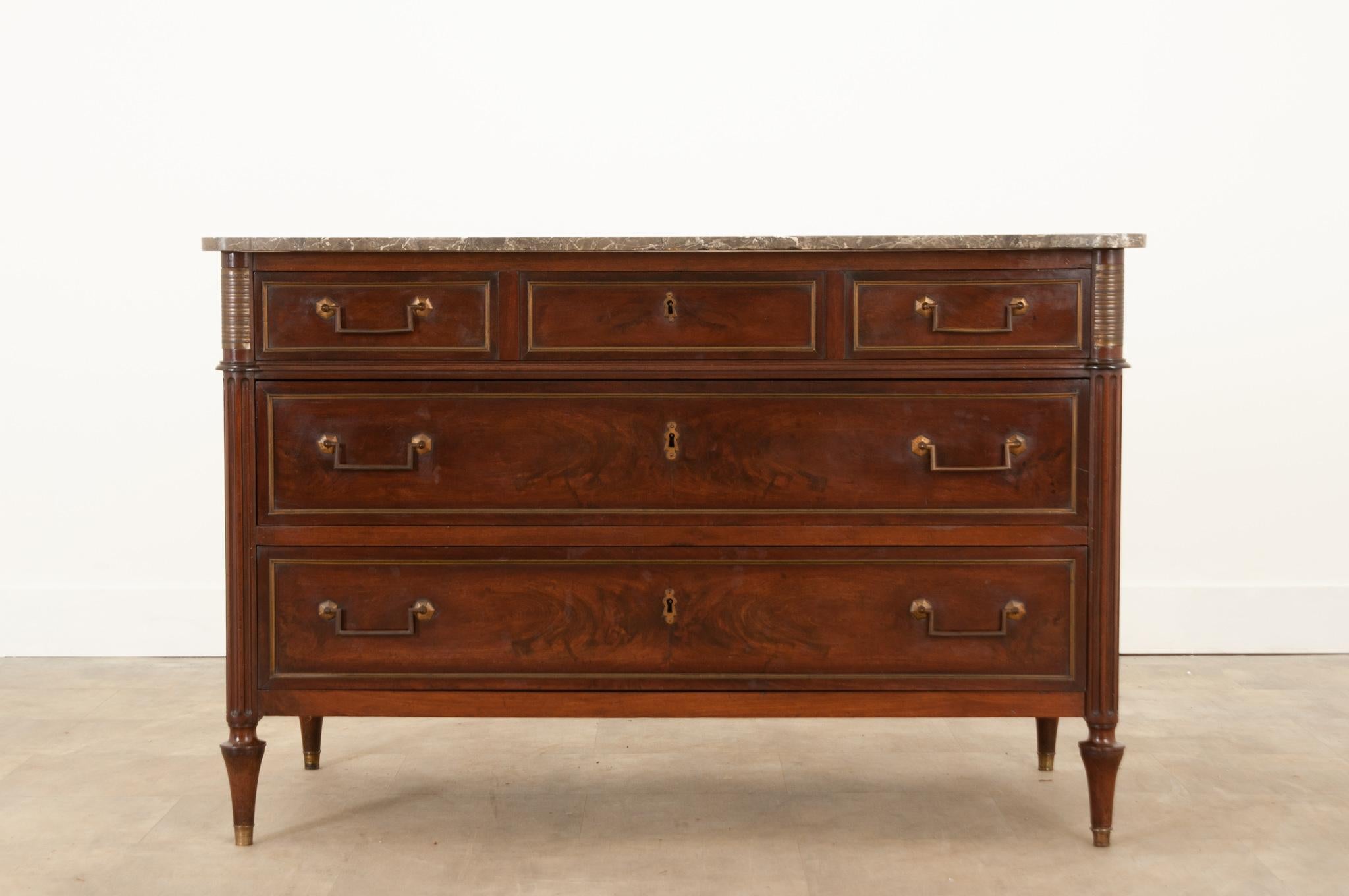 A stately Louis XVI style mahogany commode from 19th century France. Its original charcoal and white, shaped marble top is removable. A bank of three drawers are inset with brass paneling and easy to use brass hardware. The locks no longer function.