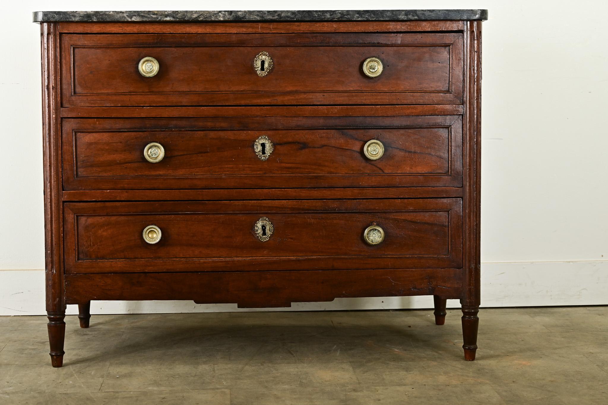 An elegant walnut & marble commode from France, 19th century, with finely carved decoration in the Louis XVI style, fitting with Empire and transitional tastes just the same. The top surface is a thick slab of a rare gray marble that has been shaped