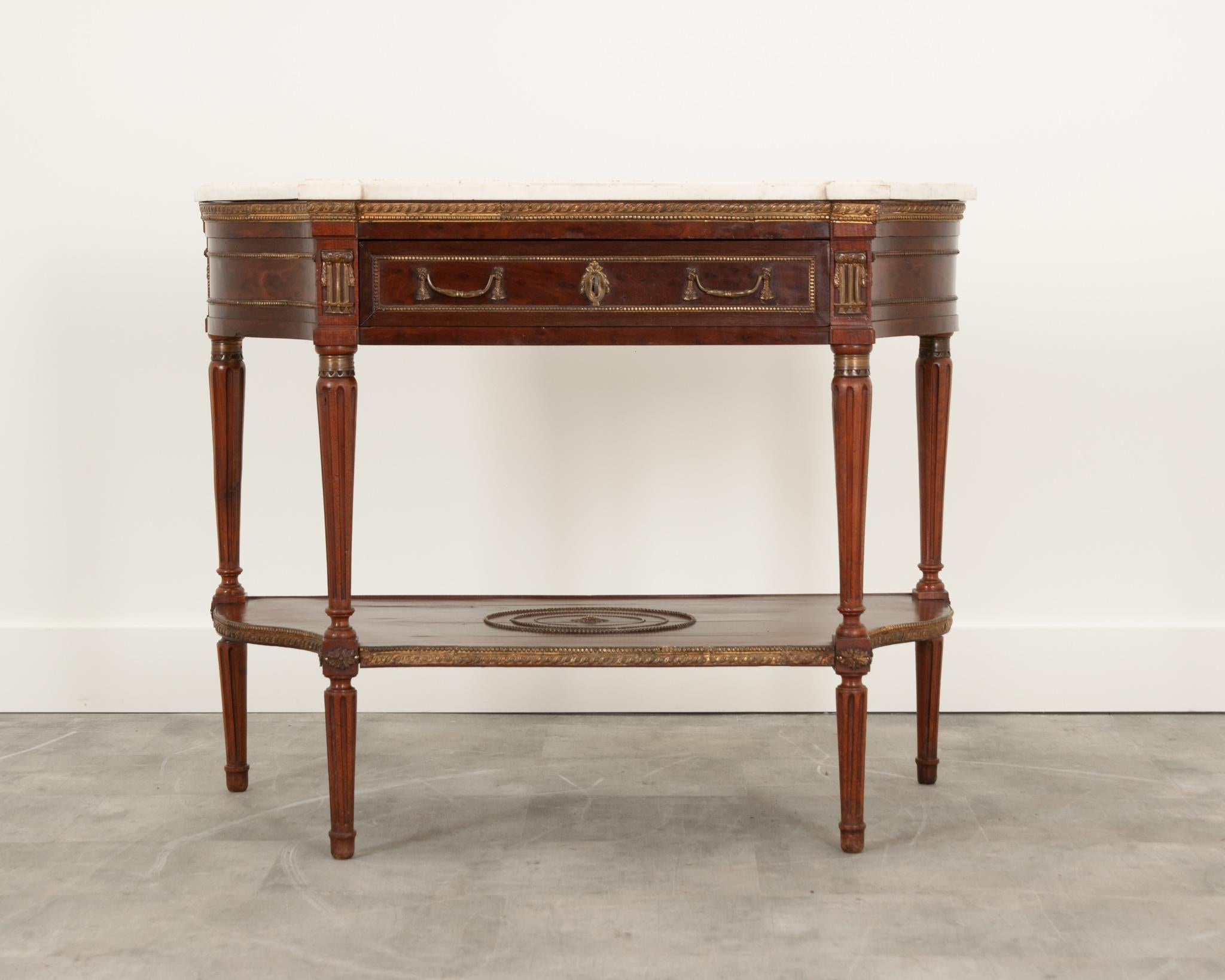This handsome French console was crafted in the 19th century in the style of Louis XVI. The original, worn shaped white marble top has a molded edge and is removable. Some stains and scuffs are visible on the tops’ surface. The apron features