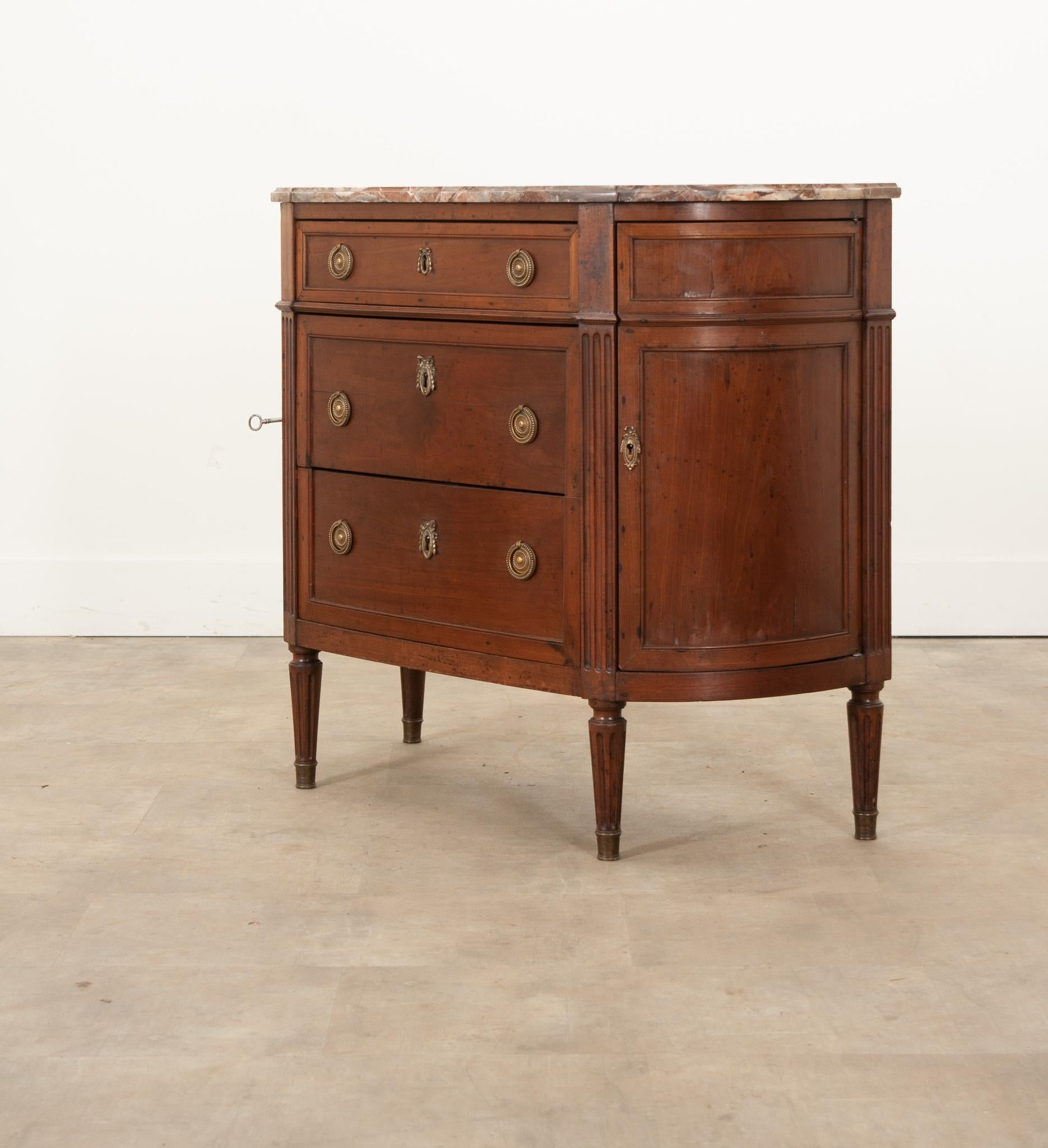 A charming French Louis XVI style commode hand-crafted in France circa 1800. This fabulous mahogany commode / buffet displays a wonderful demilune shape and is topped with its original gorgeous piece of shaped and molded marble in colors of deep