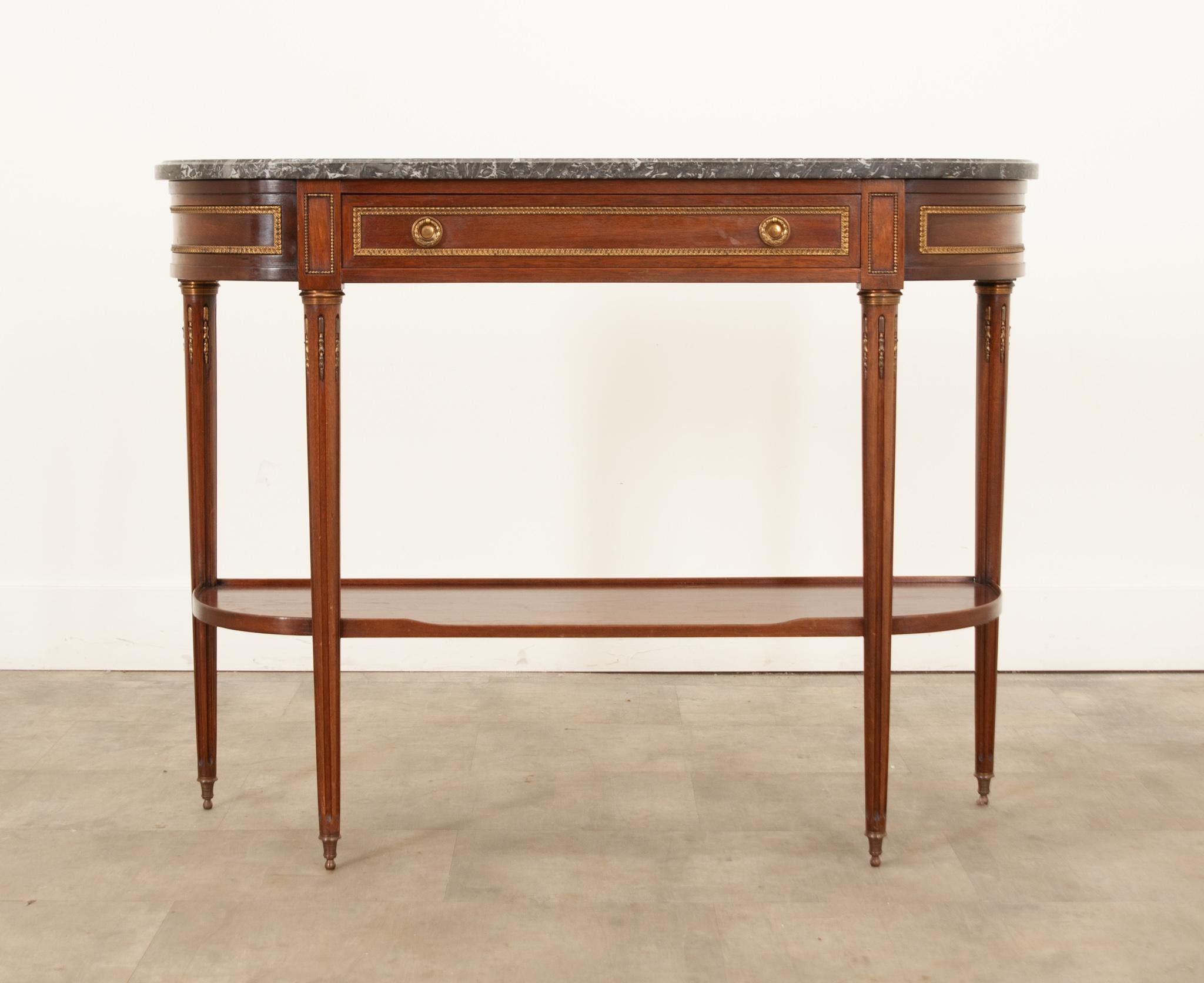 A handsome French Louis XVI style mahogany demilune console table hand-crafetd in France circa 1870. An elegant shaped marble top with a molded edge sits on top displaying wonderful patterns in variations of charcoal and white. The semi-circular top