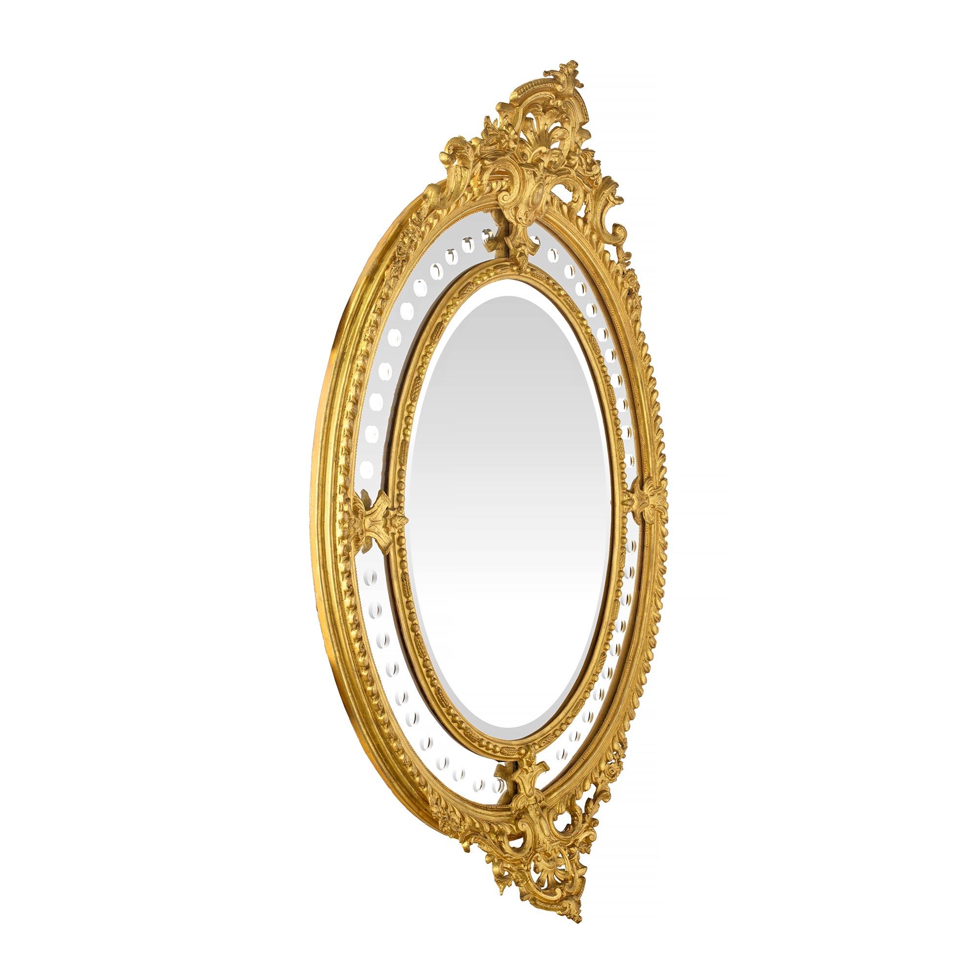 An exquisite French 19th century Louis XVI st. double framed oval giltwood mirror. The original central beveled mirror plate is framed within a dash and dart designed border. The original outer mirror panels have circular bevels throughout and are