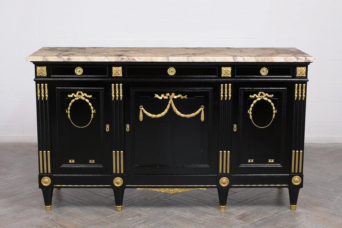 This 1880s Louis XVI style Buffet is in great condition and is made of out mahogany wood that was ebonized with a lacquered finish. The buffet features a large earth-toned marble top with a beveled edge, remarkably detailed brass molding and accents