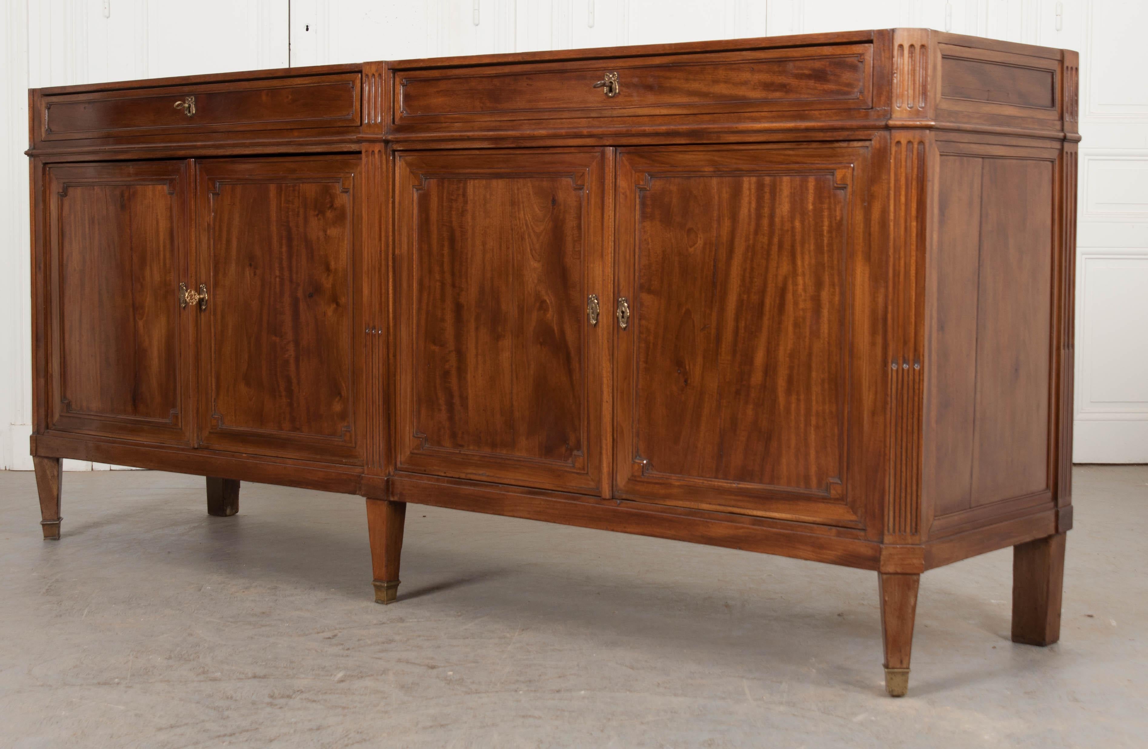 This striking Louis XVI-style mahogany enfilade, circa 1840s, is from France and features a grey marble top with white veining over a pair of long paneled drawers with gilt-brass ribbon escutcheons over four paneled doors, with like escutcheons,