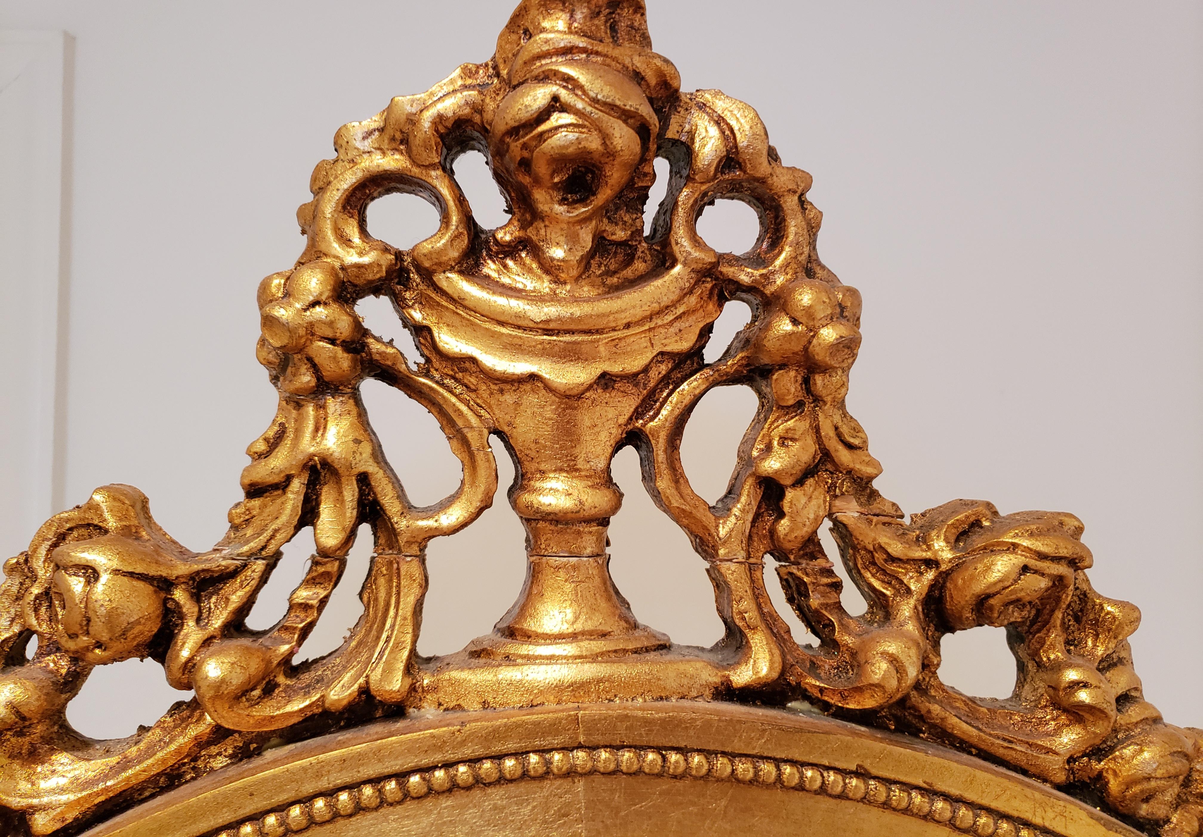 Raffinato specchio cheval francese del XIX secolo in stile Luigi XVI. La specchiera ovale è circondata da una cornice a ghirlande dorate a barbola in stile impero, affiancata da due sostegni gemelli decorati con un'urna scolpita circondata da