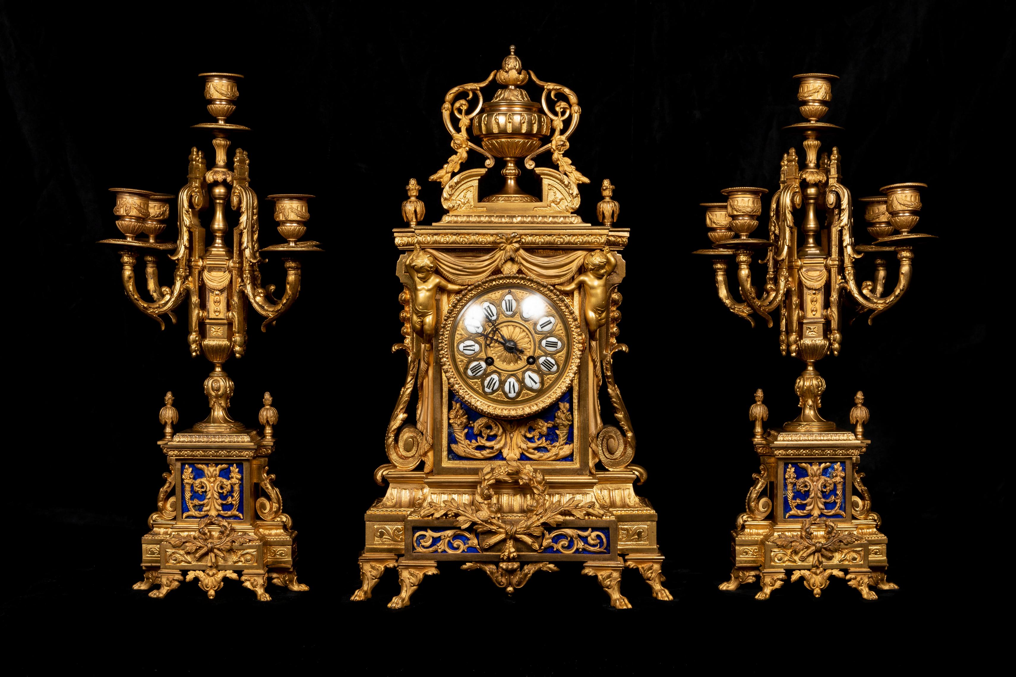 Magnifico Antique French Louis XVI Style Figural Gilt Bronze and Lapis Lazuli, un set di tre pezzi di squisita fattura con un orologio figurato centrale e una coppia di candelabri. Il superbo orologio centrale in bronzo dorato è impreziosito da due