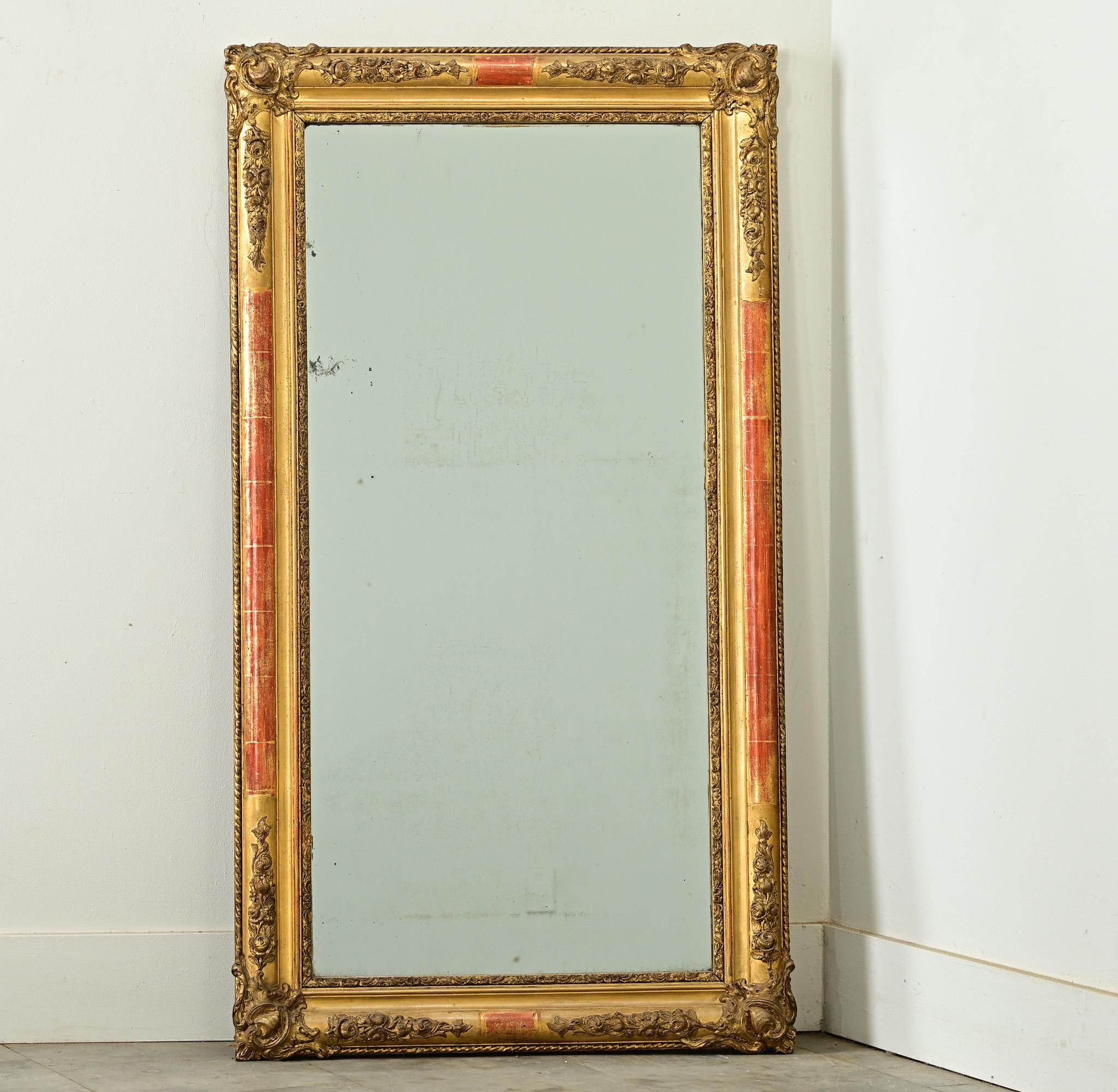 Un sorprendente specchio francese del XIX secolo in legno dorato in stile Luigi XVI che incorpora temi rococò e intagli neoclassici per animare la stretta forma rettangolare. La modanatura mostra abbondanti e dimensionali cartigli con intagli