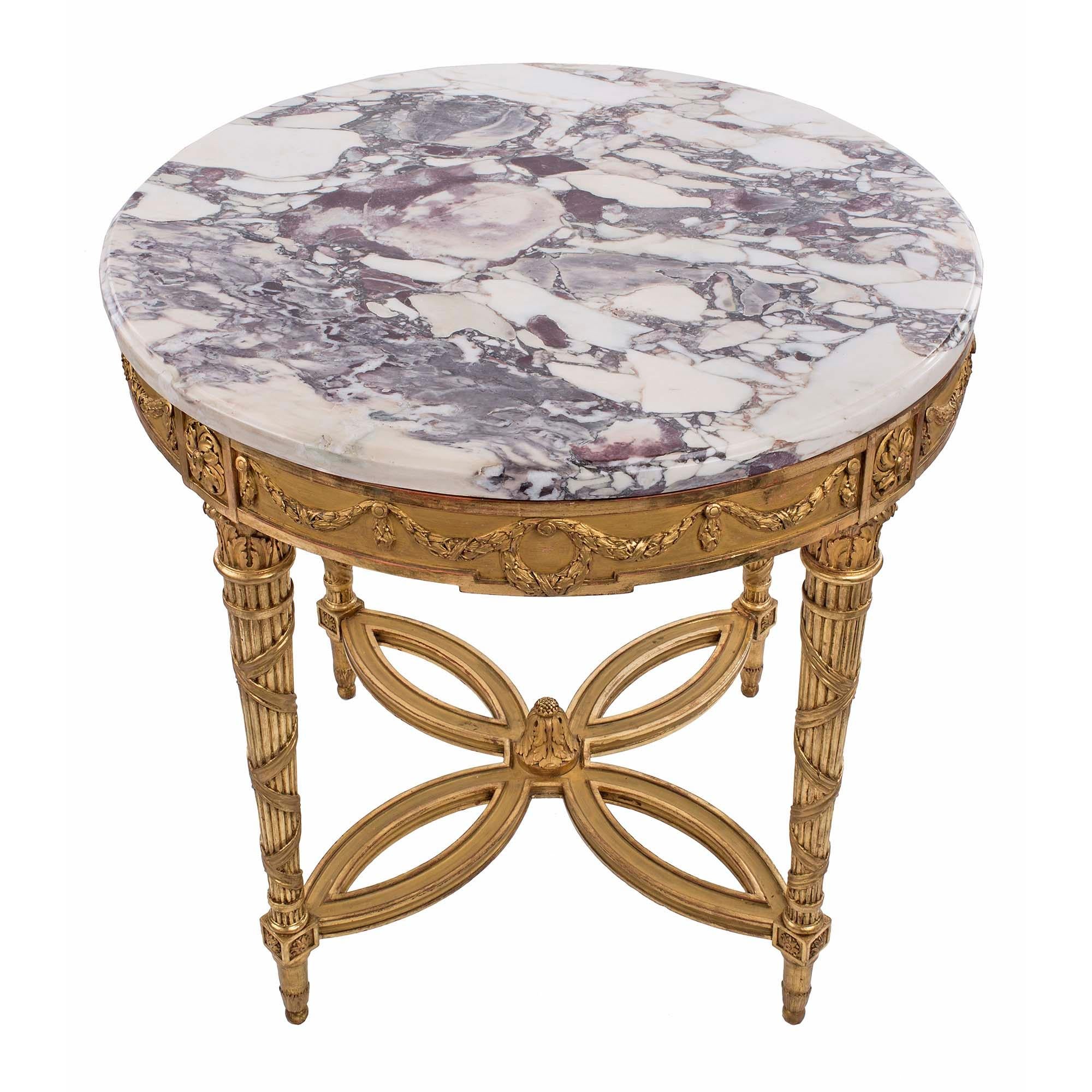 An elegant French 19th century Louis XVI st. giltwood and Brèche Médicis circular center table. The table is raised by fine topie shaped feet below richly carved block rosettes and circular tapered reeded legs. Each leg displays a tied ribbon