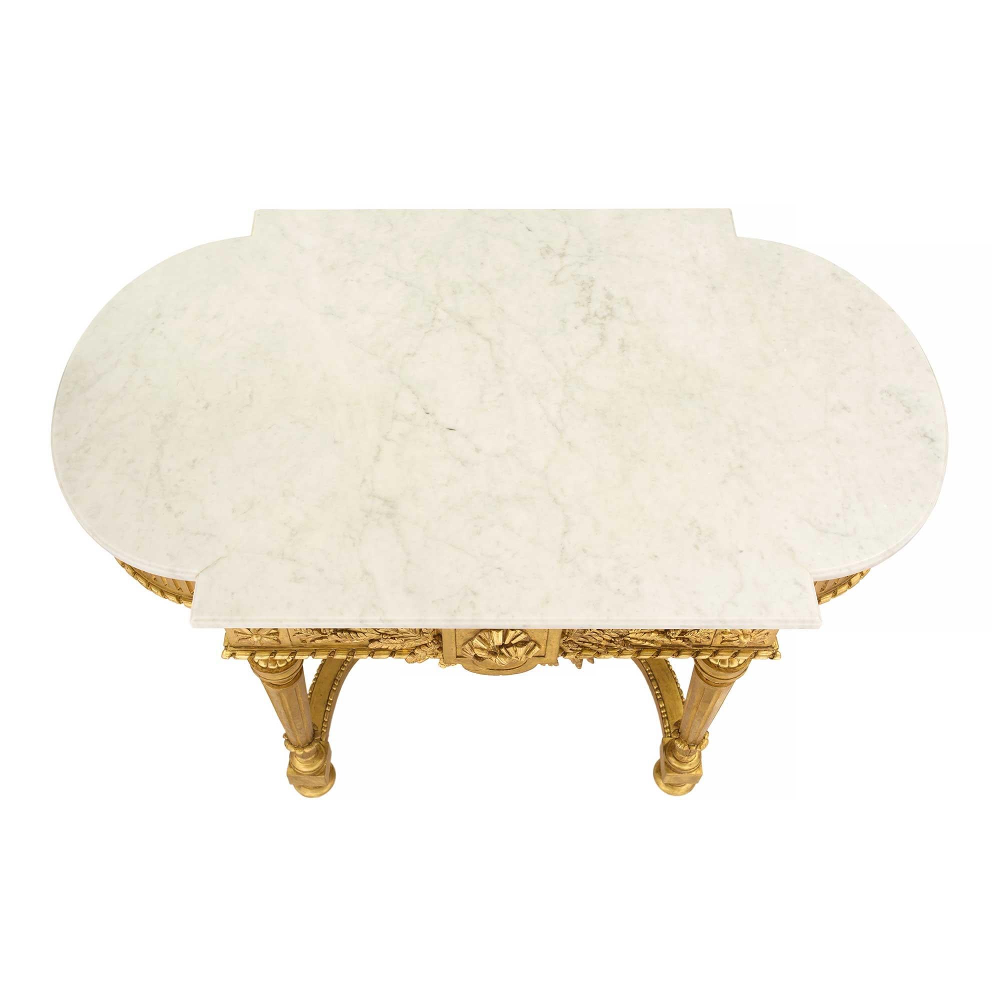An exceptional and most elegant French 19th century Louis XVI st. giltwood and white Carrara marble oval center table. The table is raised by fine topie shaped feet below circular tapered fluted legs. The legs are connected by a most impressive