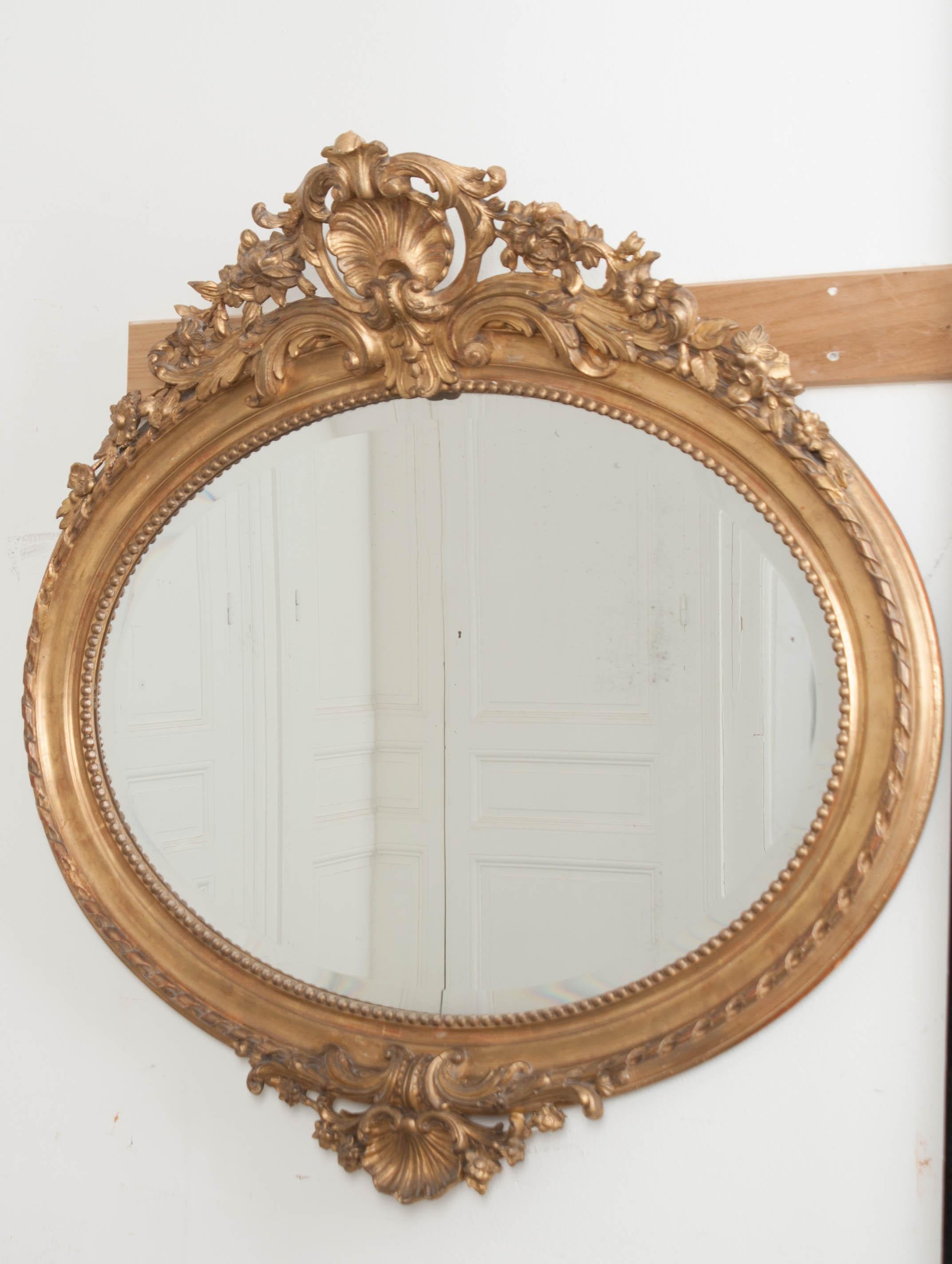 This stunning French 19th century ovoid giltwood mirror, with elaborate shell-carved crests, retains the original beveled glass mirror which displays foxing and an overall wonderful patina!