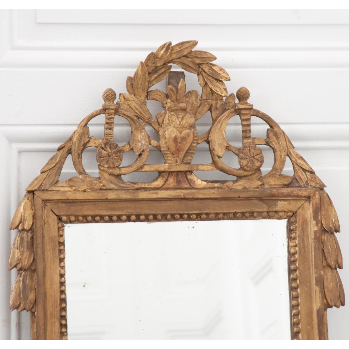 A beautifully carved petite giltwood mirror. This mirror has a wonderful crest that features a heart at its center with foliate carvings, scrolled filigree and acanthus leaves. The original glass remains intact and adds great character with some