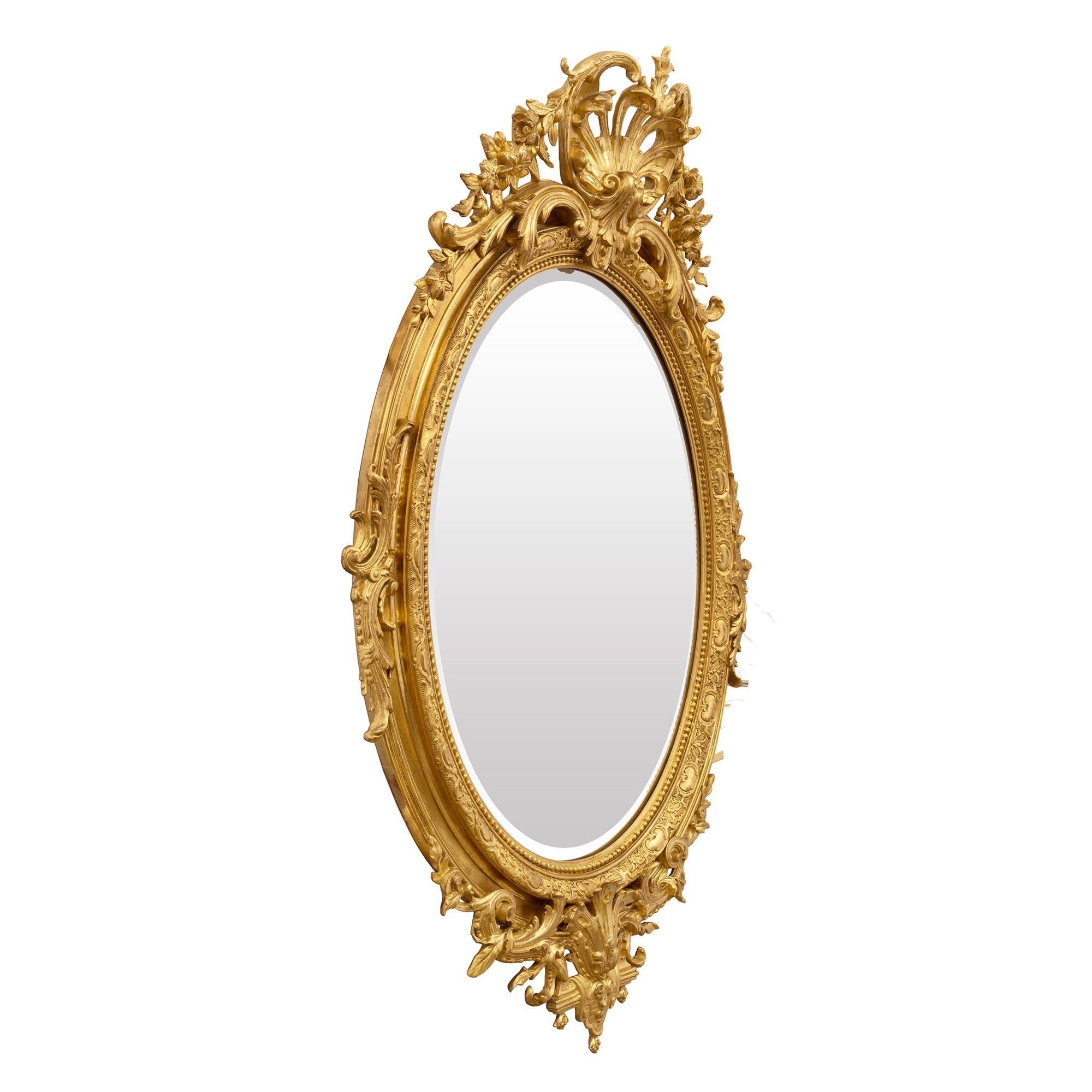 A most elegant French 19th century Louis XVI st. giltwood oval mirror. The original beveled mirror plate is framed within a fine beaded giltwood border and beautiful decorative foliate carved movements. At the base are exceptional scrolled foliate