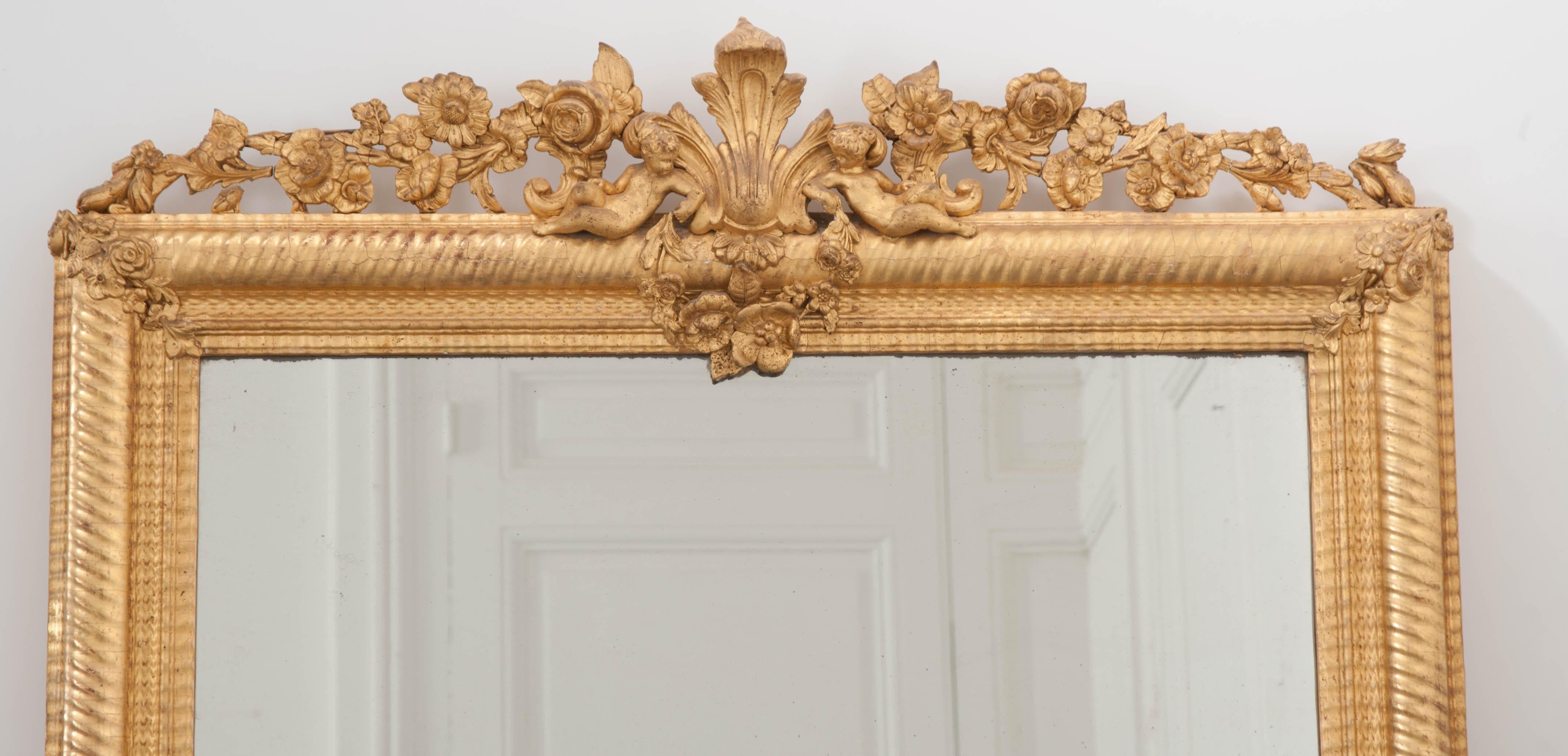 This beautiful gilded over mantel mirror, in the Louis XVI style, is from France, circa 1860. It features a delicate crest with central anthemion flanked by two cherubs among flowering vines which rests atop the wavy ribbed frame. The original