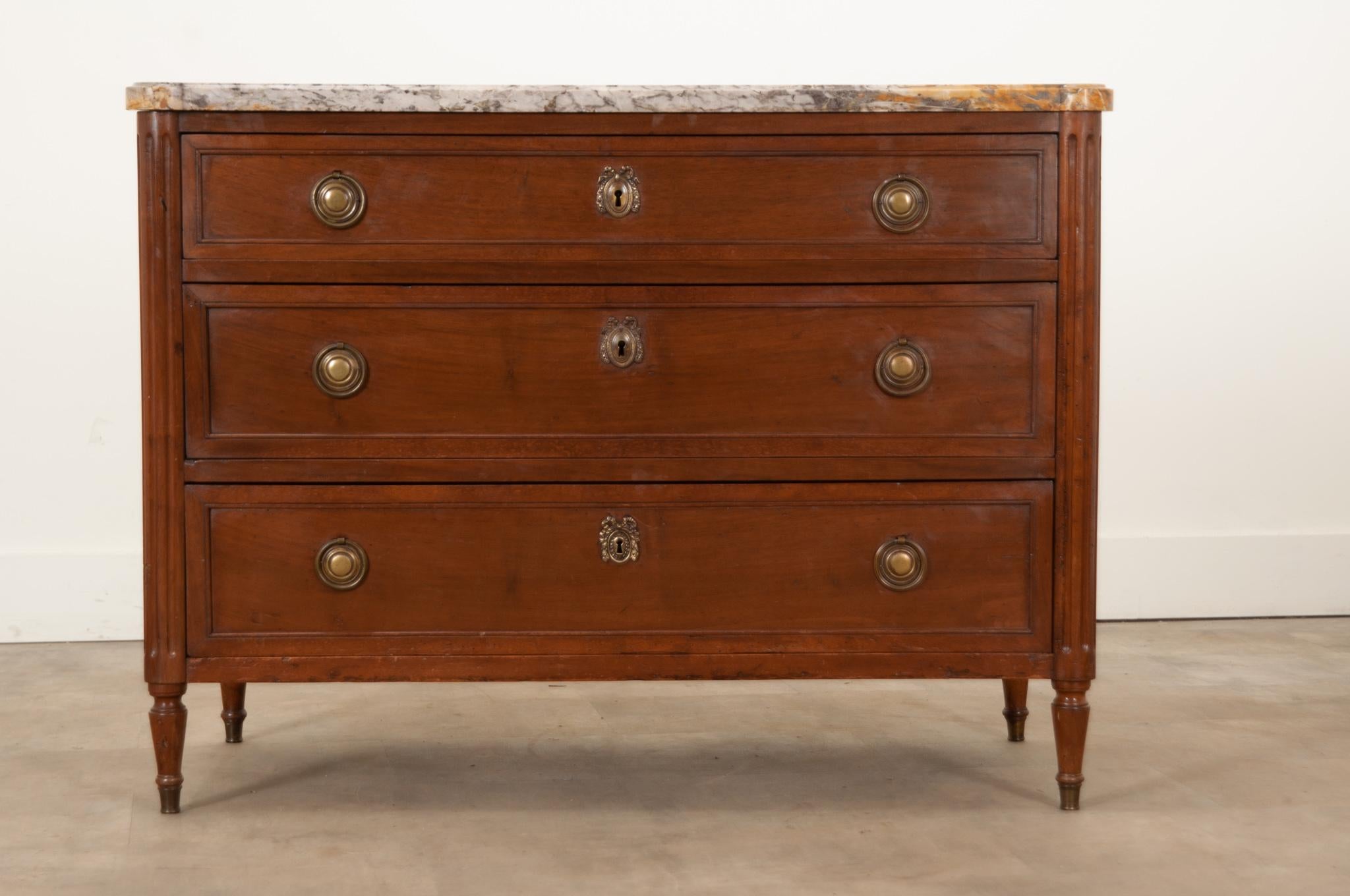 A French 19th Century Louis XVI style commode made of beautiful mahogany and topped with its original show-stopping piece of marble. Hand-crafted in France circa 1830, its shaped marble top contains the most beautiful colors of ochre, charcoal, and