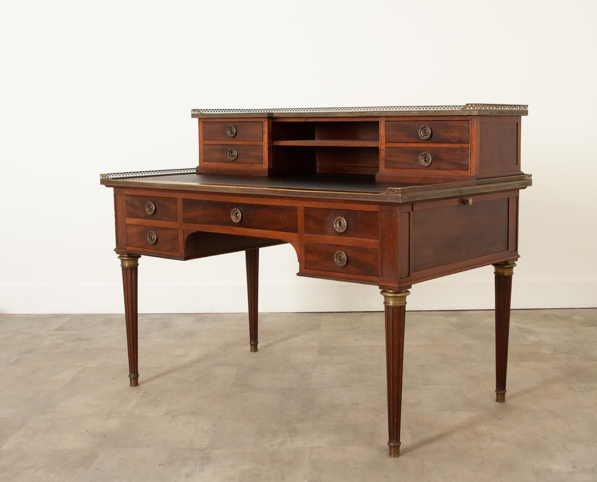 A wonderful mid-19th century French Louis XVI style mahogany desk hand-crafted in France circa 1850.  A beautiful, smooth top of flame mahogany is surrounded by a three quarter decorative brass gallery following down to two open center storage