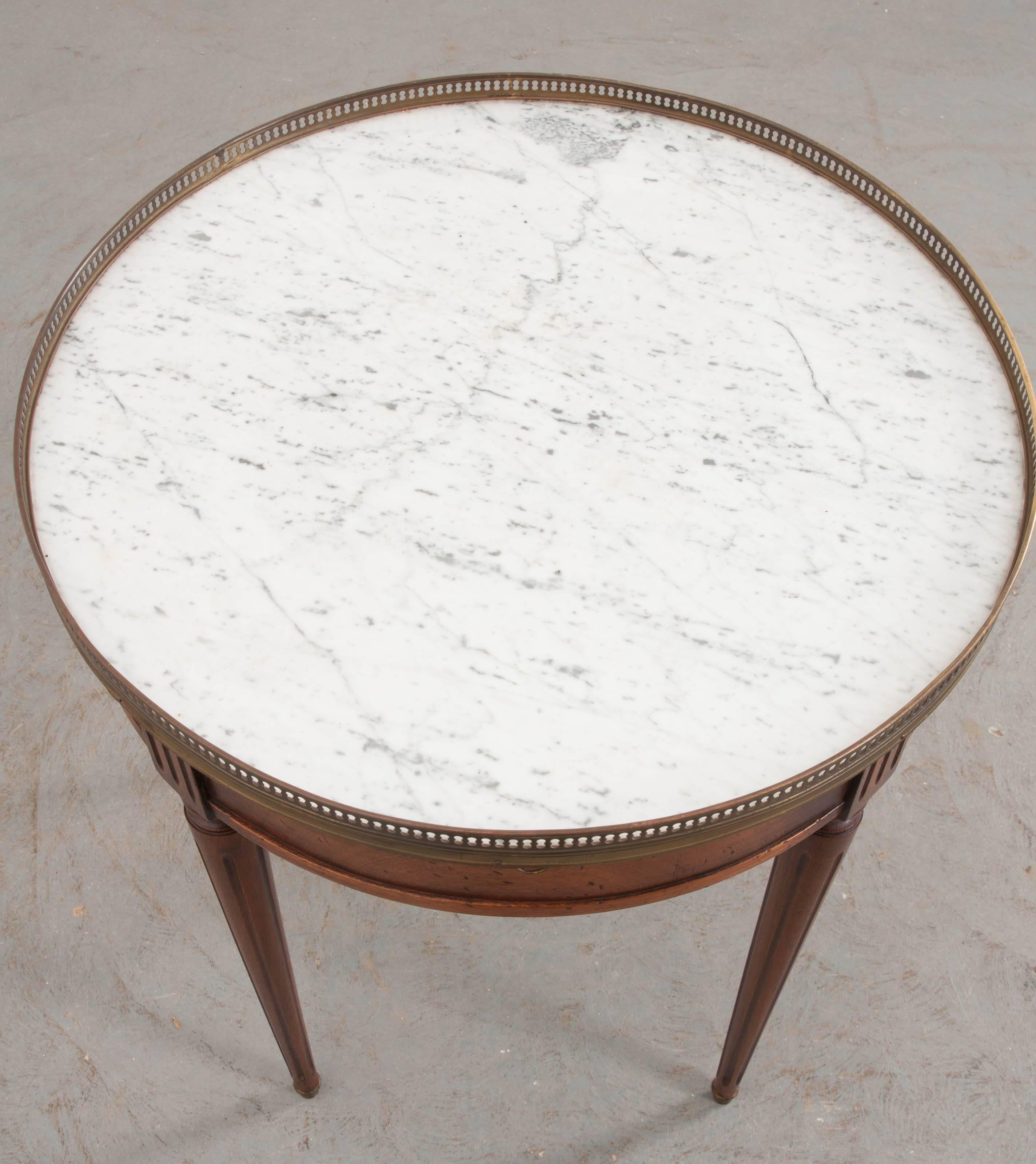 This Louis XVI style gueridon was made in France, at the end of the 19th century, using exceptional mahogany and marble. The table features a beautiful white, round marble top, with grey speckles, that is encircled by a pierced brass gallery. The