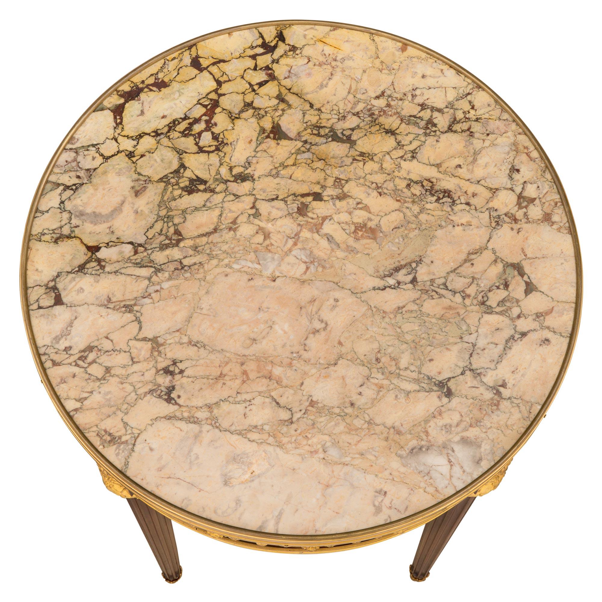 Très élégante table d'appoint française du XIXe siècle, de style Louis XVI, en acajou, bronze doré et marbre Sarrancolin. La table circulaire est surélevée par de minces pieds circulaires fuselés et cannelés, avec de jolis sabots feuillagés en forme