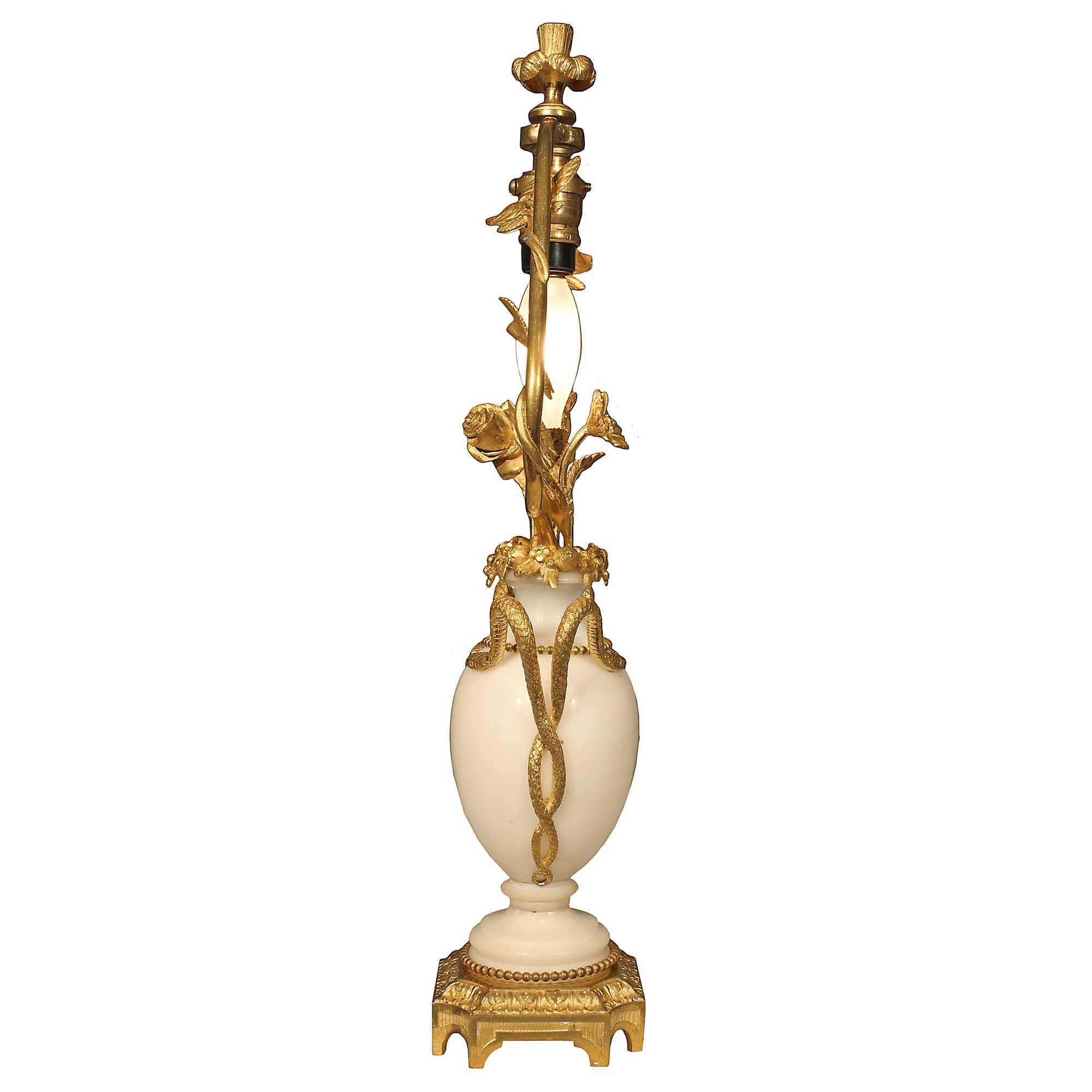 A charming French 19th century Louis XVI st. small scale white Carrera marble and ormolu lamp. The lamp is raised on a square ormolu base with concave corners, a fluted and coeur pattern in a satin and burnished finish. The white Carrara marble body