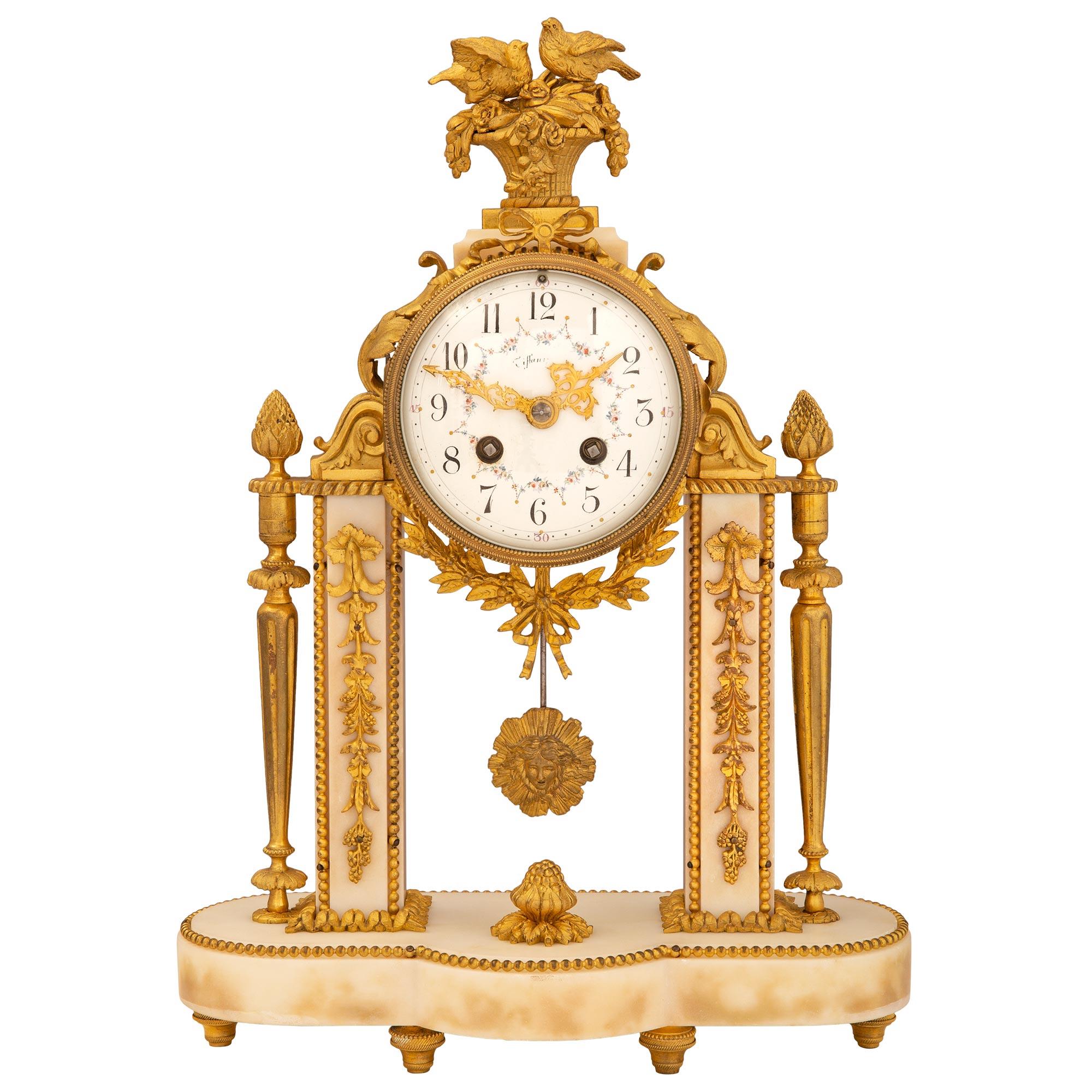 Une exquise horloge de style Louis XVI du 19ème siècle en marbre blanc de Carrare et bronze doré, signée 'Tiffany'. Il repose sur une base en marbre avec des supports en forme de topie en bronze doré. Au-dessus se trouvent deux colonnes décorées par