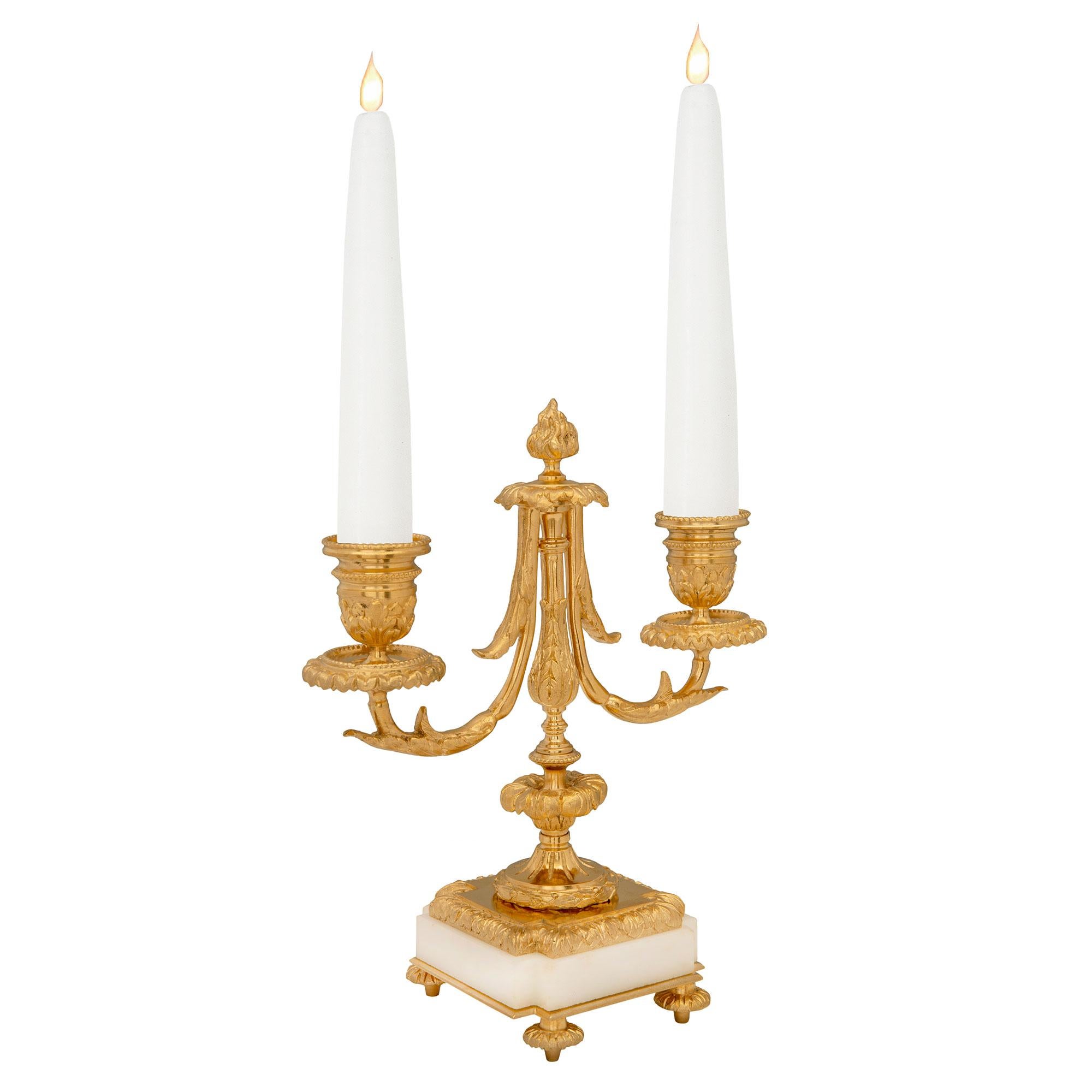 Une charmante et très élégante paire de candélabres à deux bras en marbre blanc de Carrare et bronze doré de style Louis XVI du 19ème siècle. Chaque candélabre est surélevé par de fins pieds en forme de topie, sous de remarquables bases carrées en