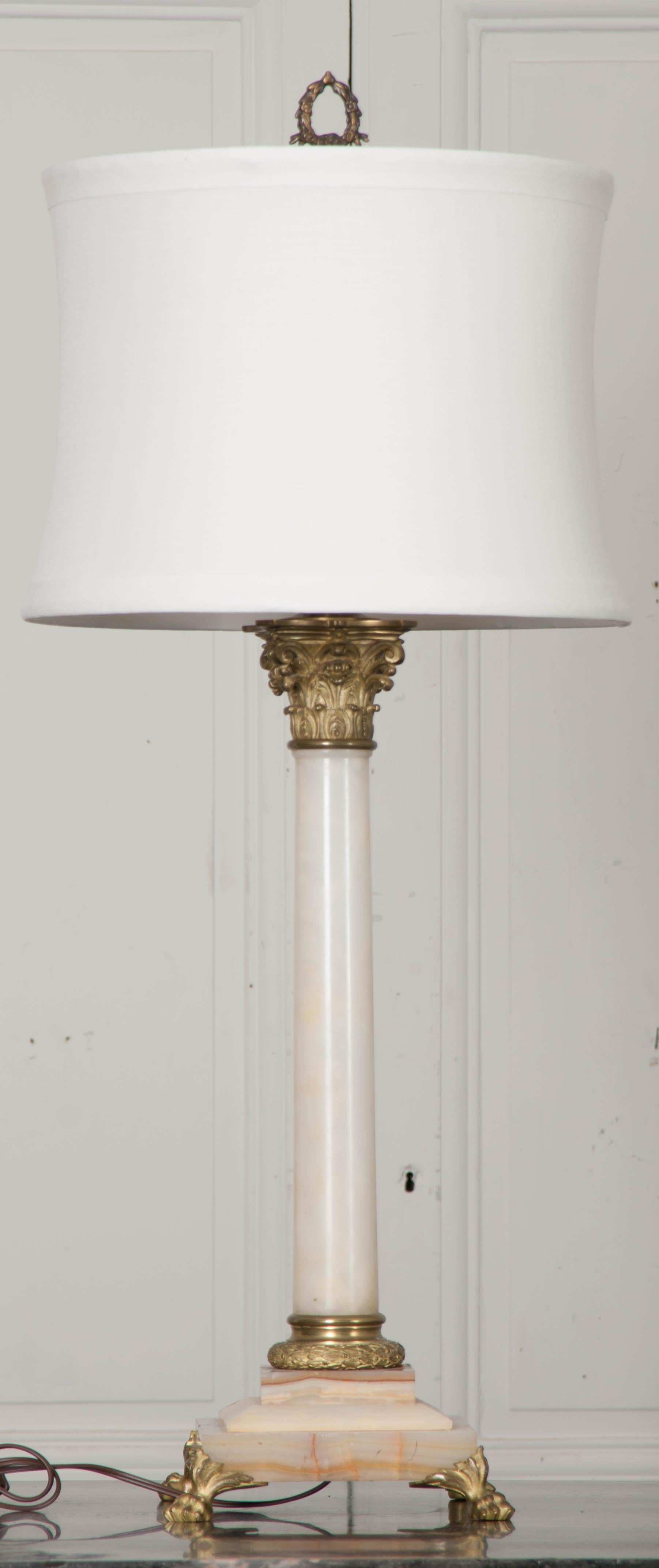 A stunning solid marble, column-form oil lamp base that has been electrified for use as an impressive table lamp. The Corinthian style column is ivory in color, with beautiful rust-colored veins, and rests on a stacked marble base. The gilt brass